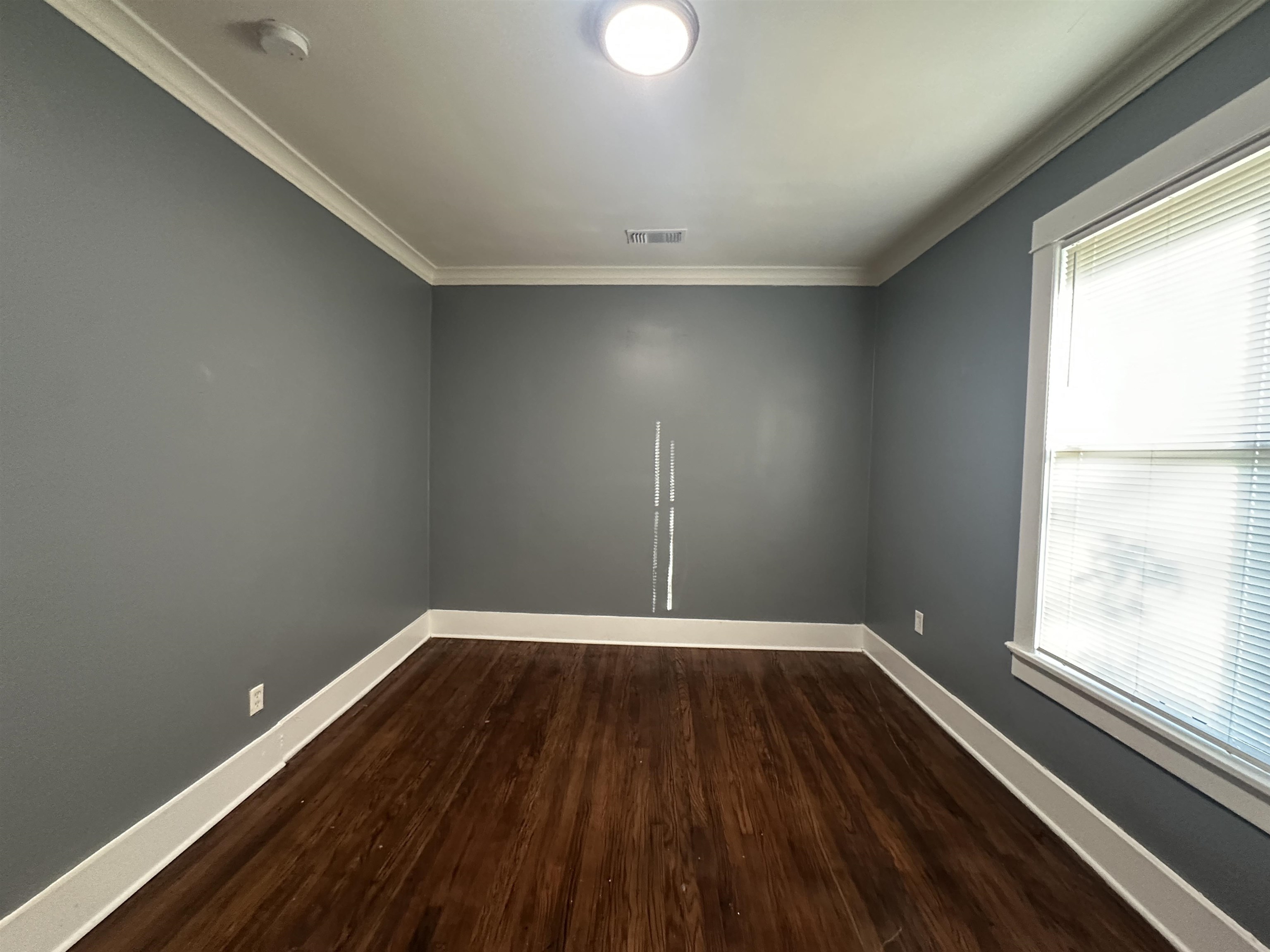 Empty room with dark hardwood / wood-style floors, crown molding, and a healthy amount of sunlight