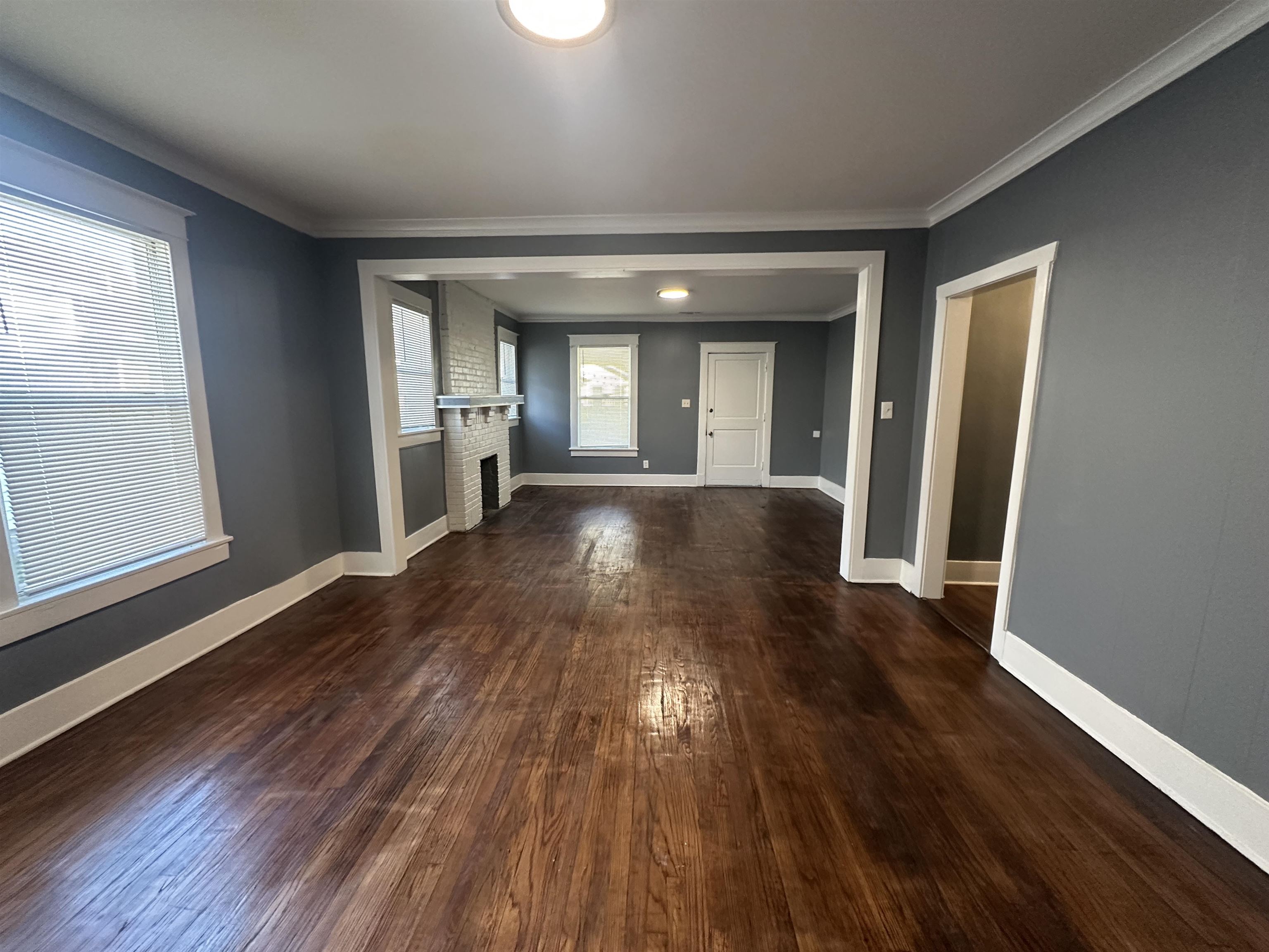 Unfurnished living room with a brick fireplace, dark wood-type flooring, and crown molding