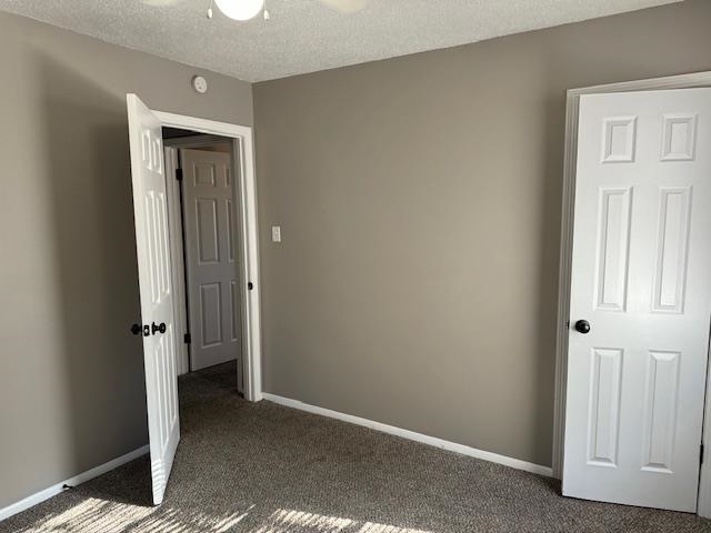 Unfurnished bedroom featuring dark colored carpet, a textured ceiling, and ceiling fan