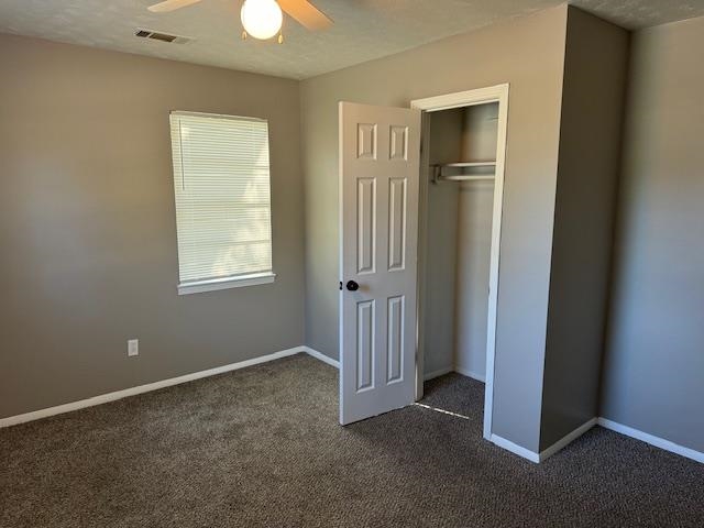 Unfurnished bedroom with ceiling fan, dark carpet, a textured ceiling, and a closet