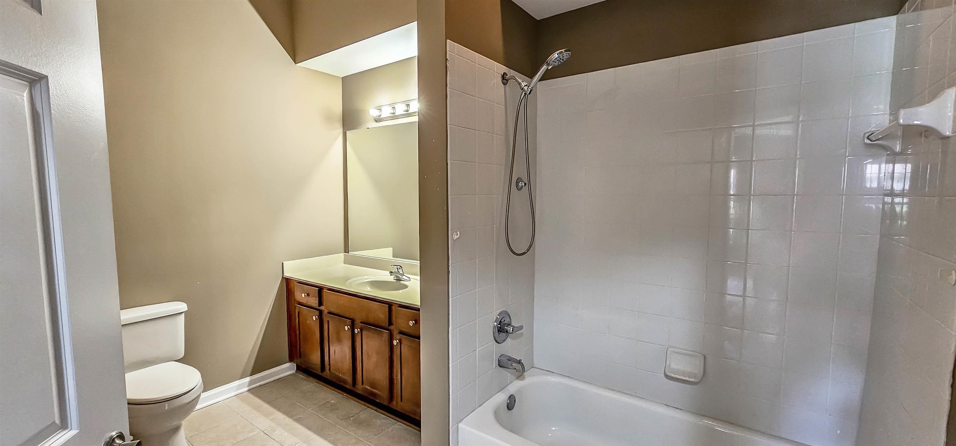 Full bathroom with toilet, tile patterned floors, vanity, and tiled shower / bath combo