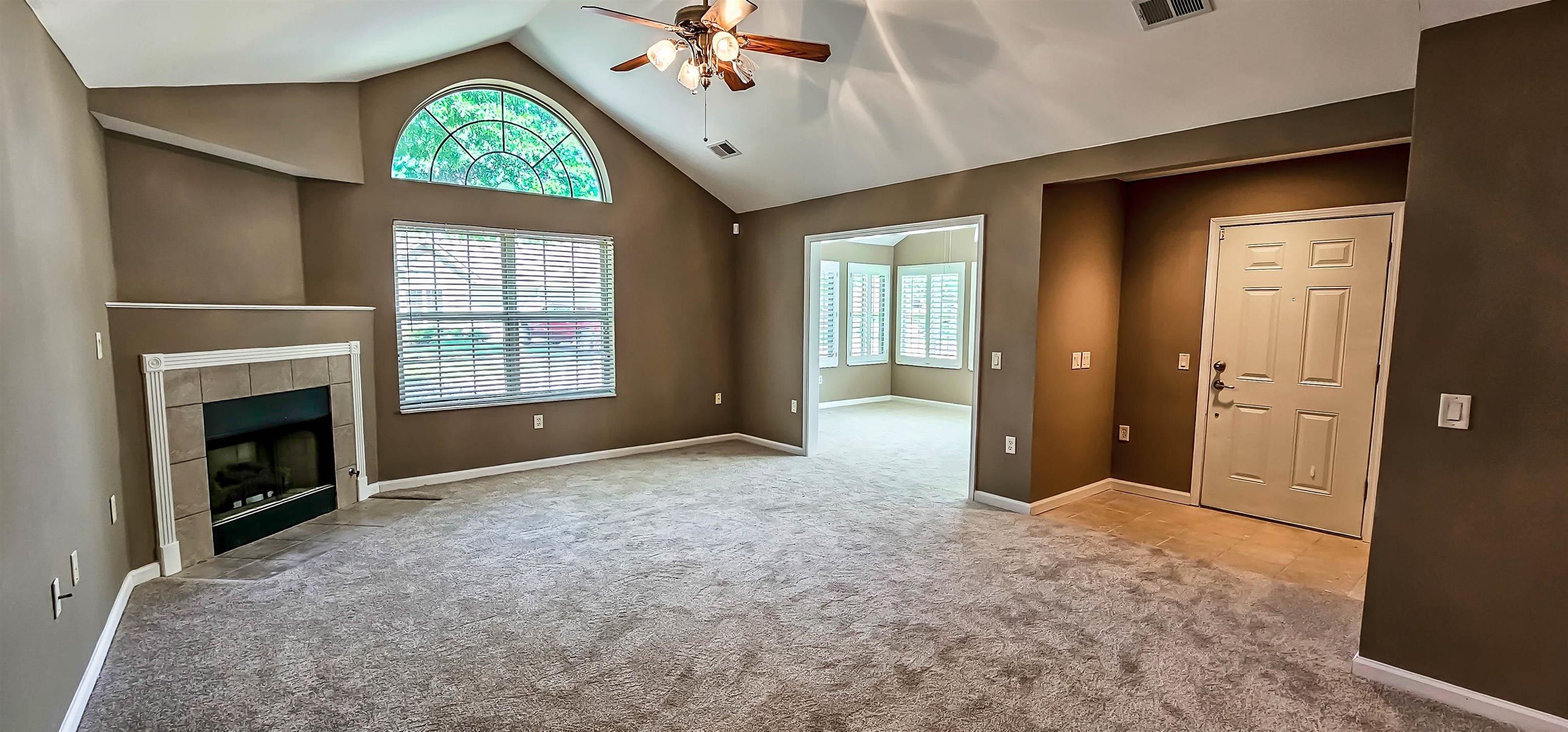 Unfurnished living room featuring ceiling fan, a fireplace, high vaulted ceiling, and light carpet