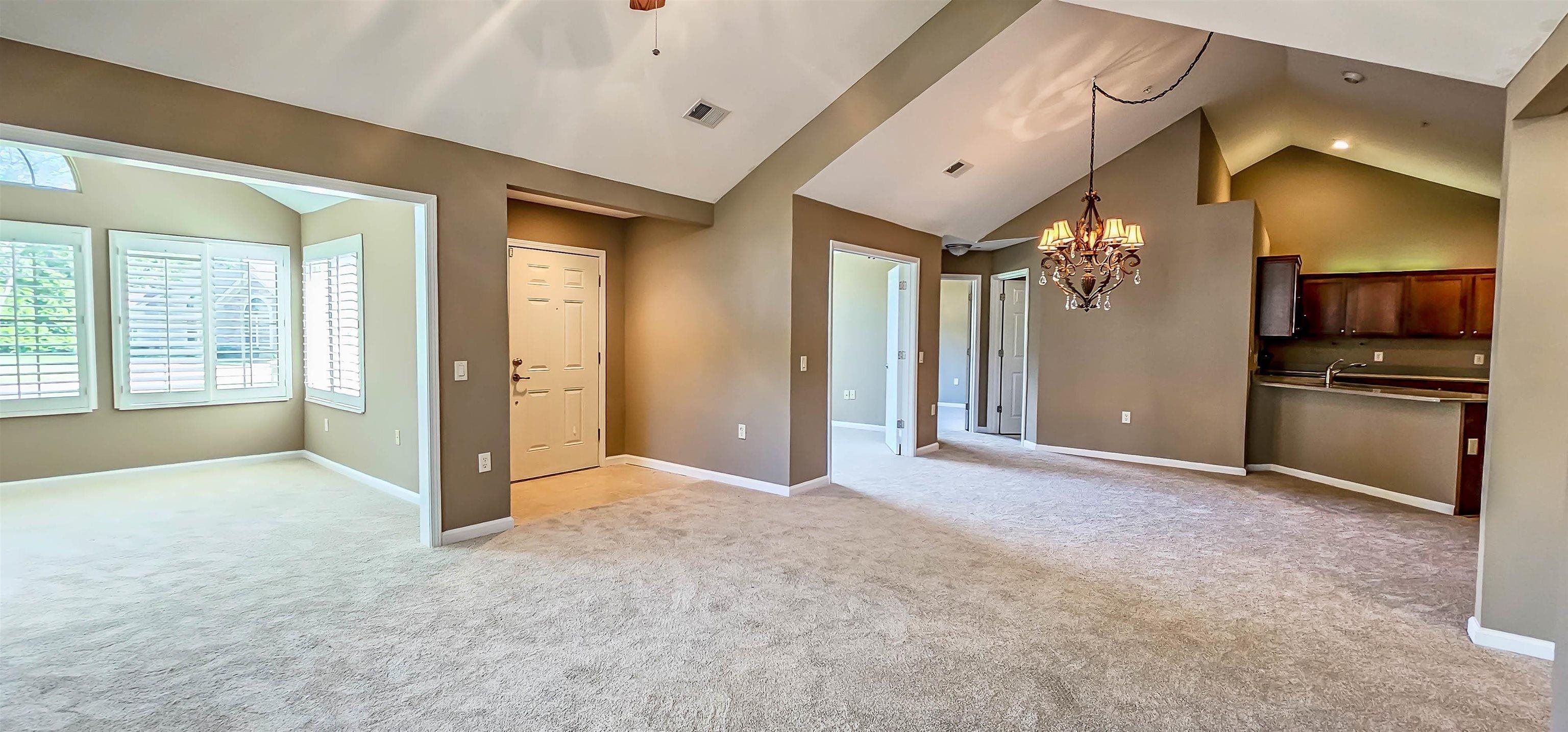 Unfurnished living room with light colored carpet, lofted ceiling, and an inviting chandelier