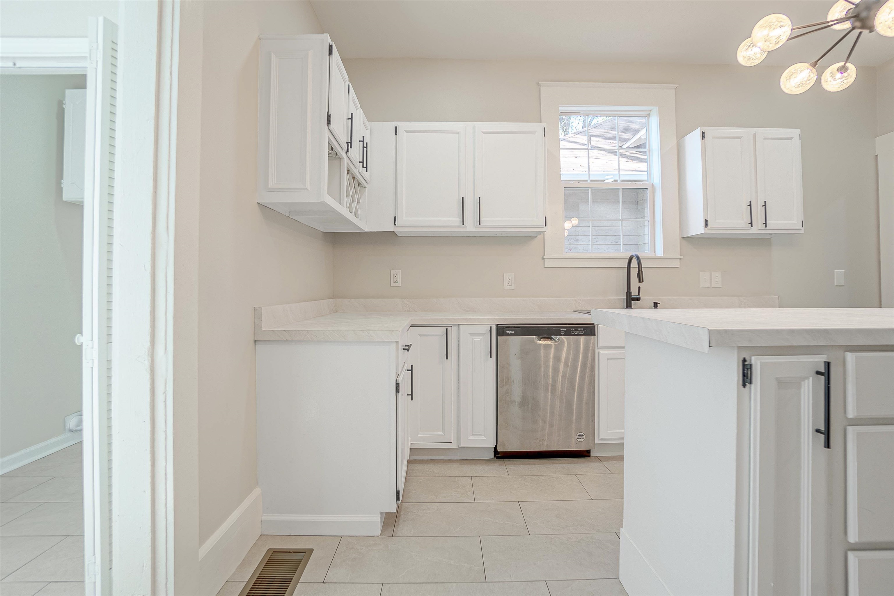 Kitchen with white cabinets, light tile patterned floors, a chandelier, and stainless steel dishwasher