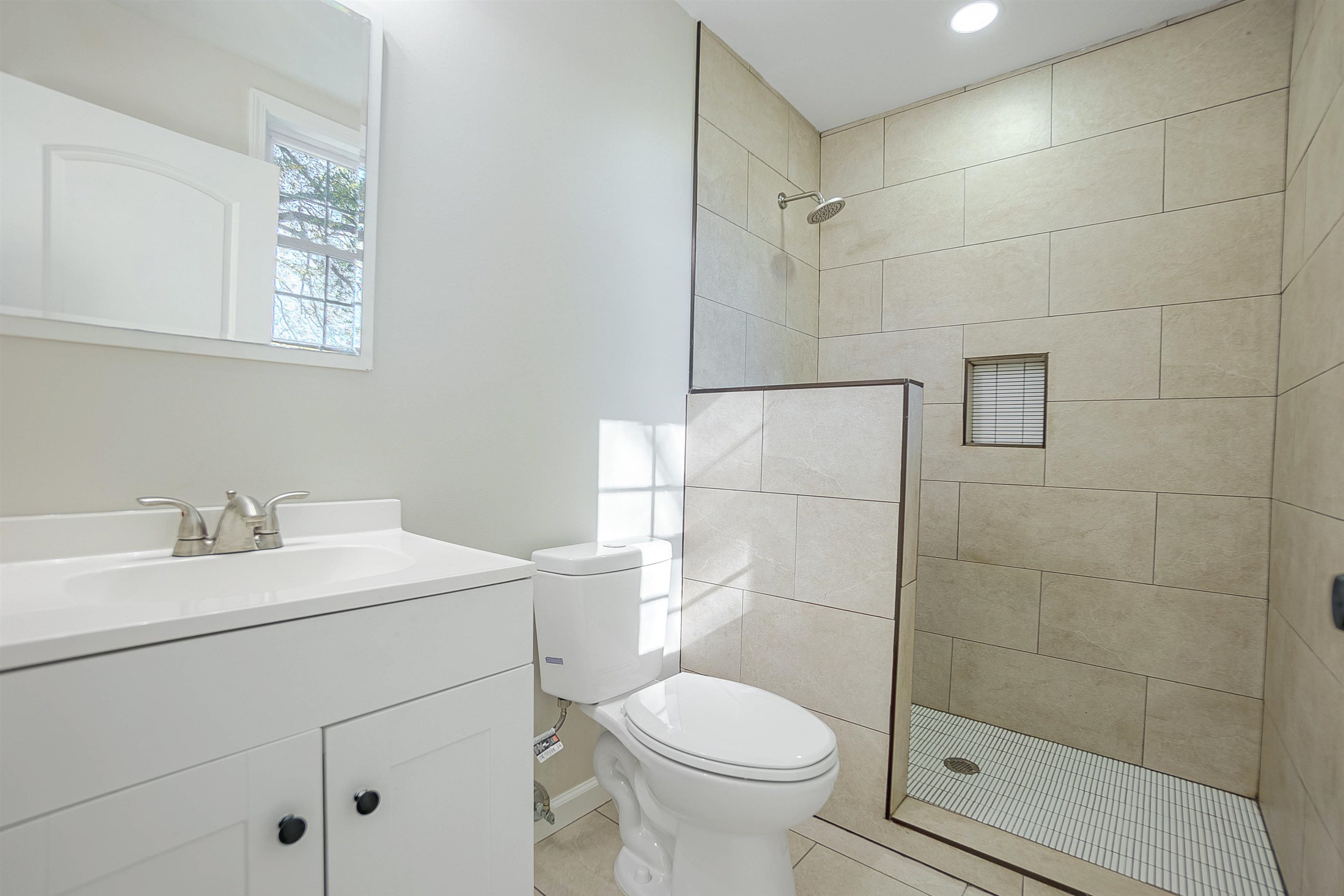 Bathroom with a tile shower, tile patterned flooring, vanity, and toilet
