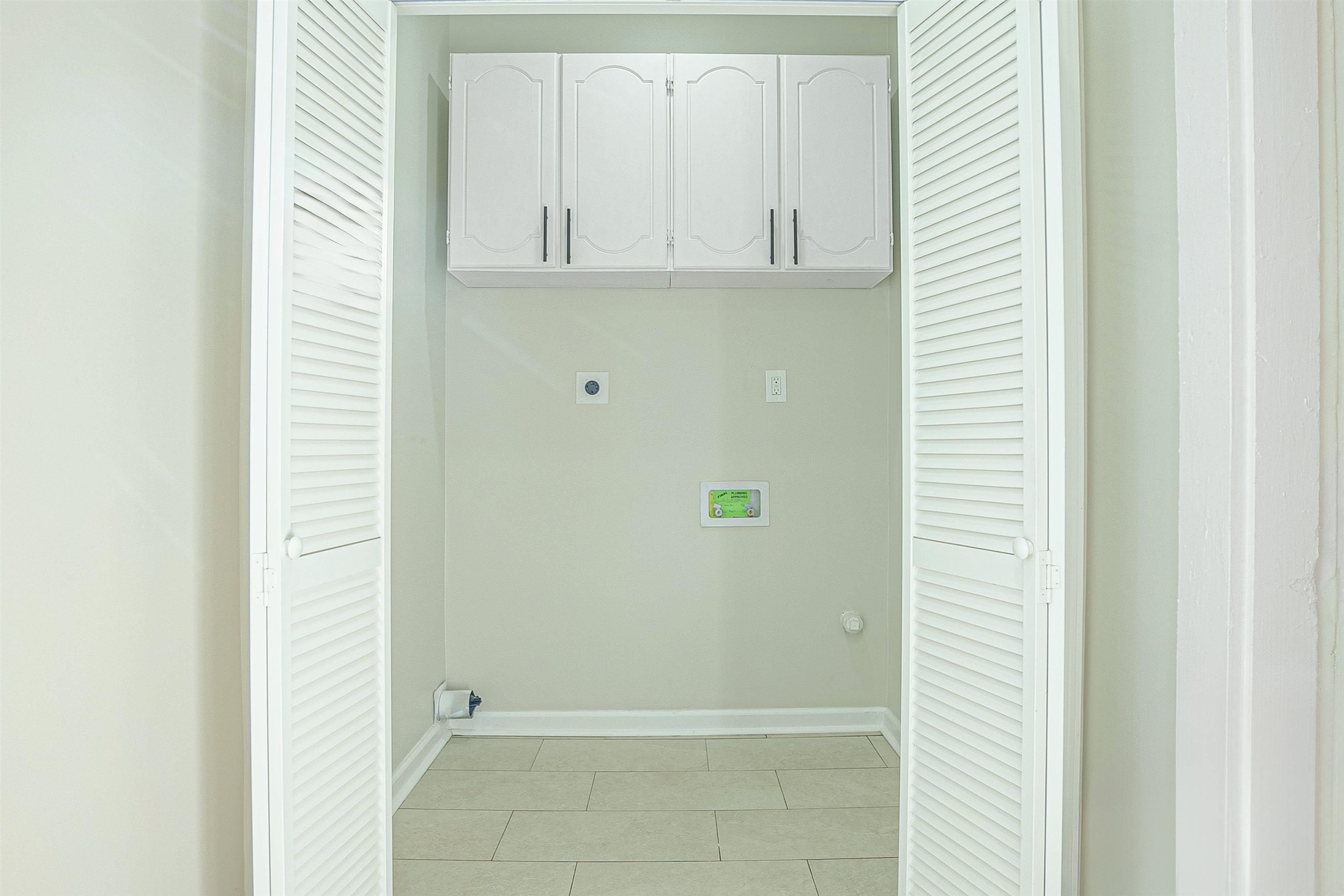 Washroom featuring electric dryer hookup, light tile patterned flooring, and cabinets
