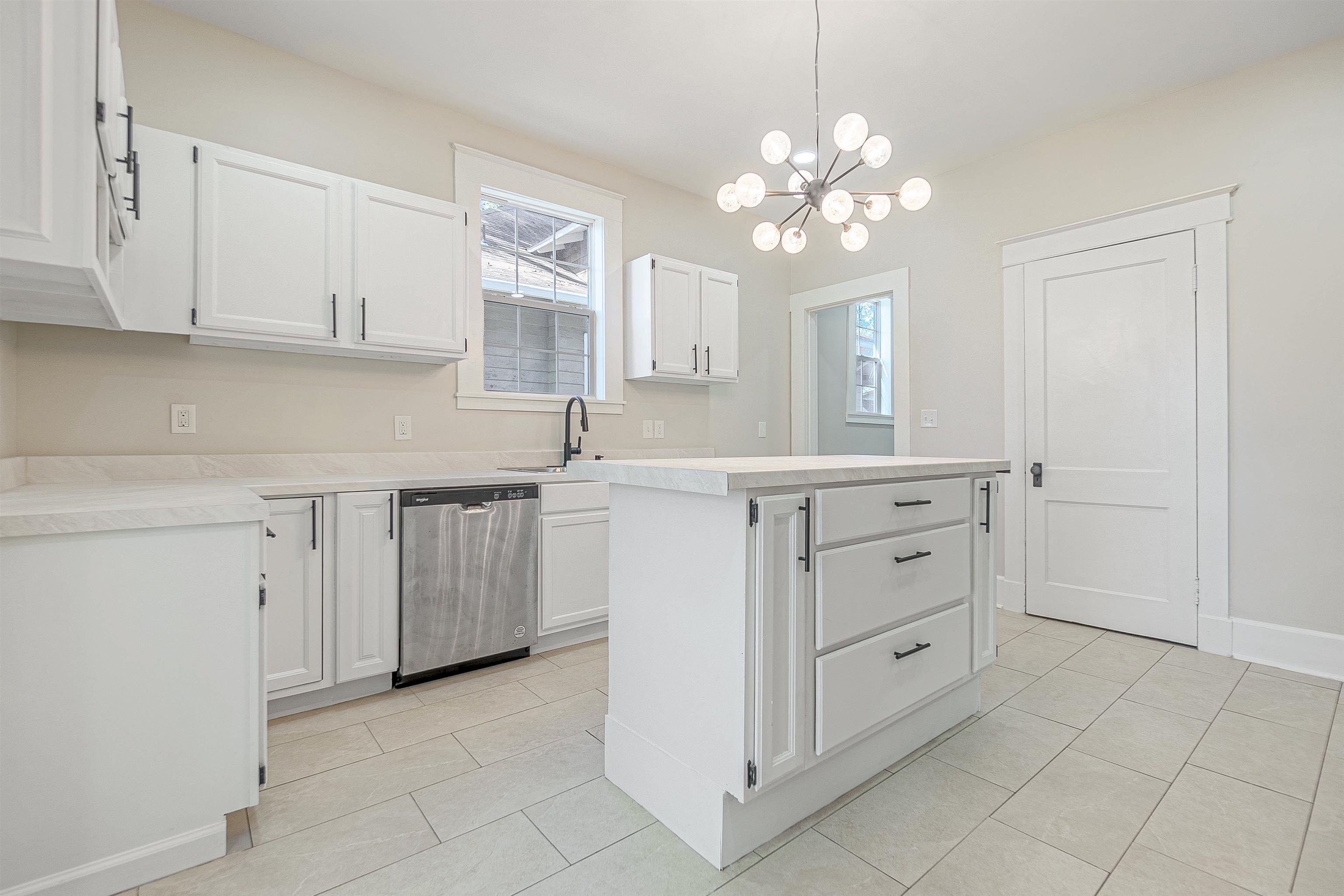 Kitchen with a healthy amount of sunlight, white cabinetry, stainless steel dishwasher, and a notable chandelier