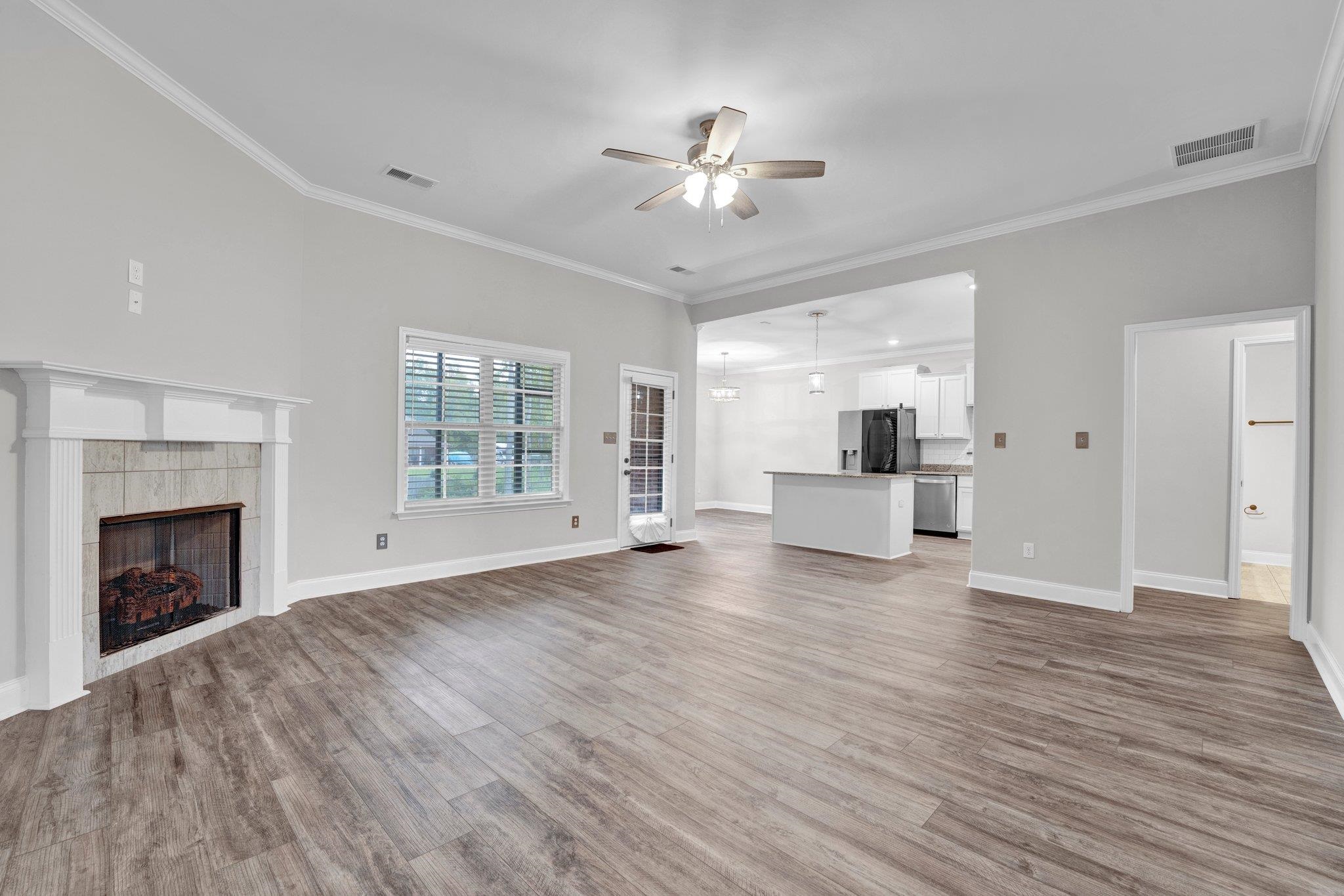 Unfurnished living room with ceiling fan, light wood-type flooring, ornamental molding, and a tile fireplace