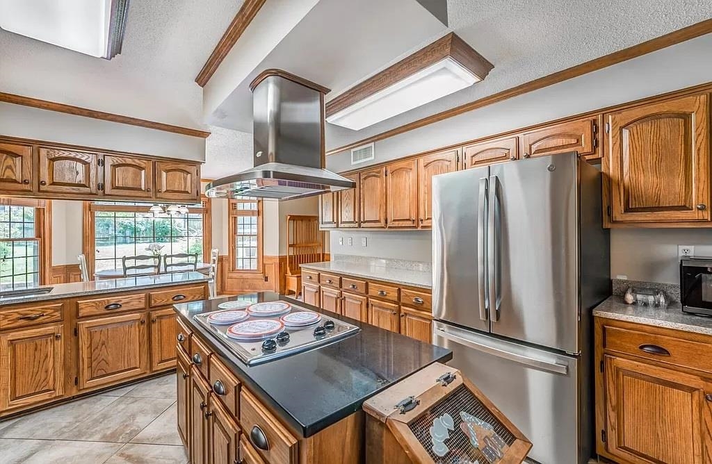 Kitchen with a textured ceiling, stainless steel appliances, ornamental molding, and island range hood