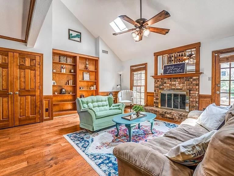 Living room with high vaulted ceiling, ceiling fan, light wood-type flooring, a fireplace, and beamed ceiling