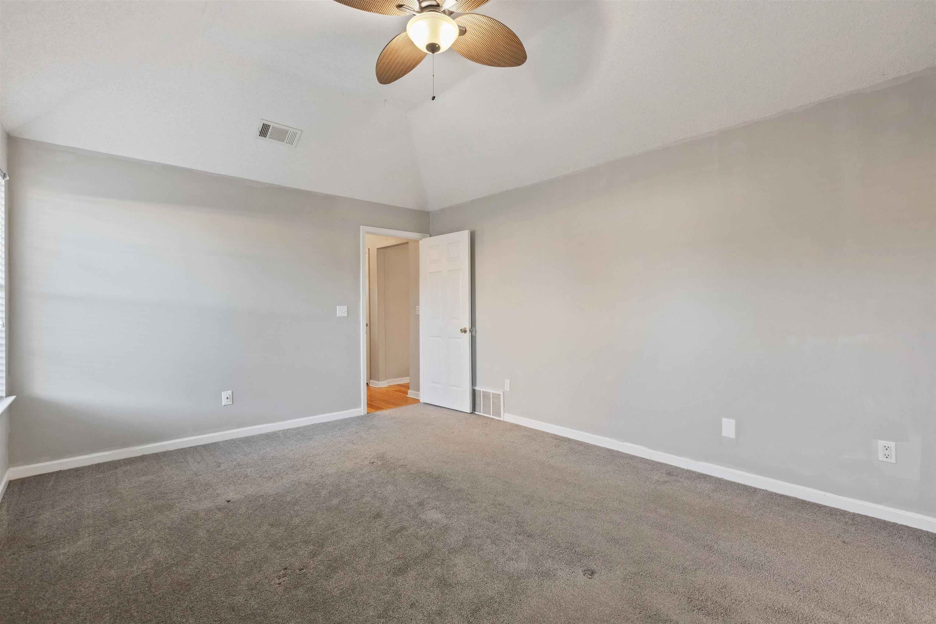 Carpeted empty room featuring ceiling fan and lofted ceiling