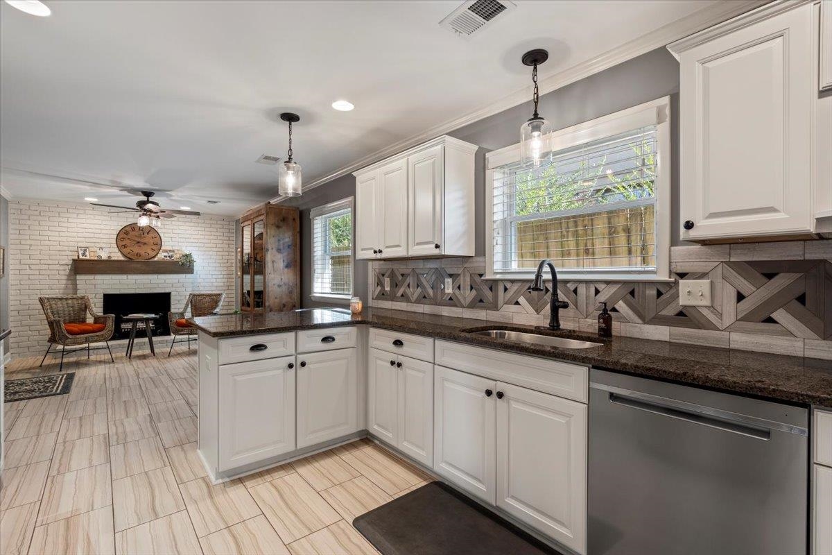 Kitchen with white cabinets, sink, hanging light fixtures, stainless steel dishwasher, and kitchen peninsula