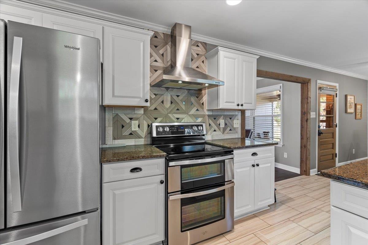 Kitchen featuring white cabinets, dark stone countertops, wall chimney exhaust hood, and appliances with stainless steel finishes