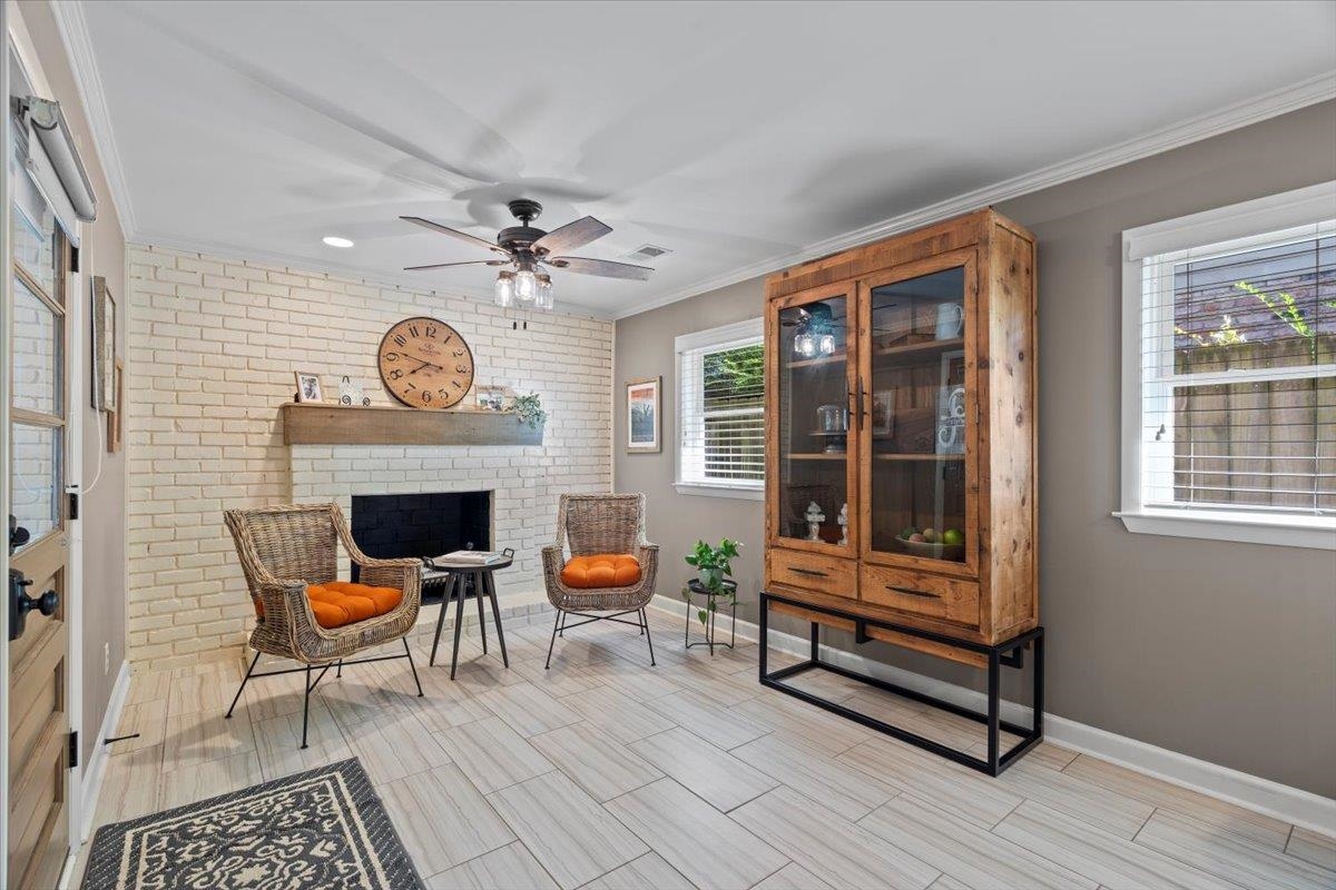Sitting room featuring crown molding, a fireplace, ceiling fan, and brick wall