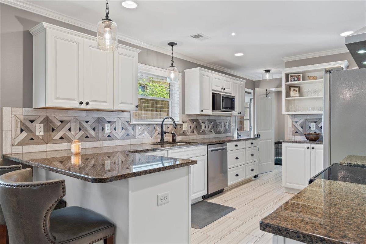 Kitchen featuring a kitchen breakfast bar, stainless steel appliances, sink, decorative light fixtures, and white cabinetry