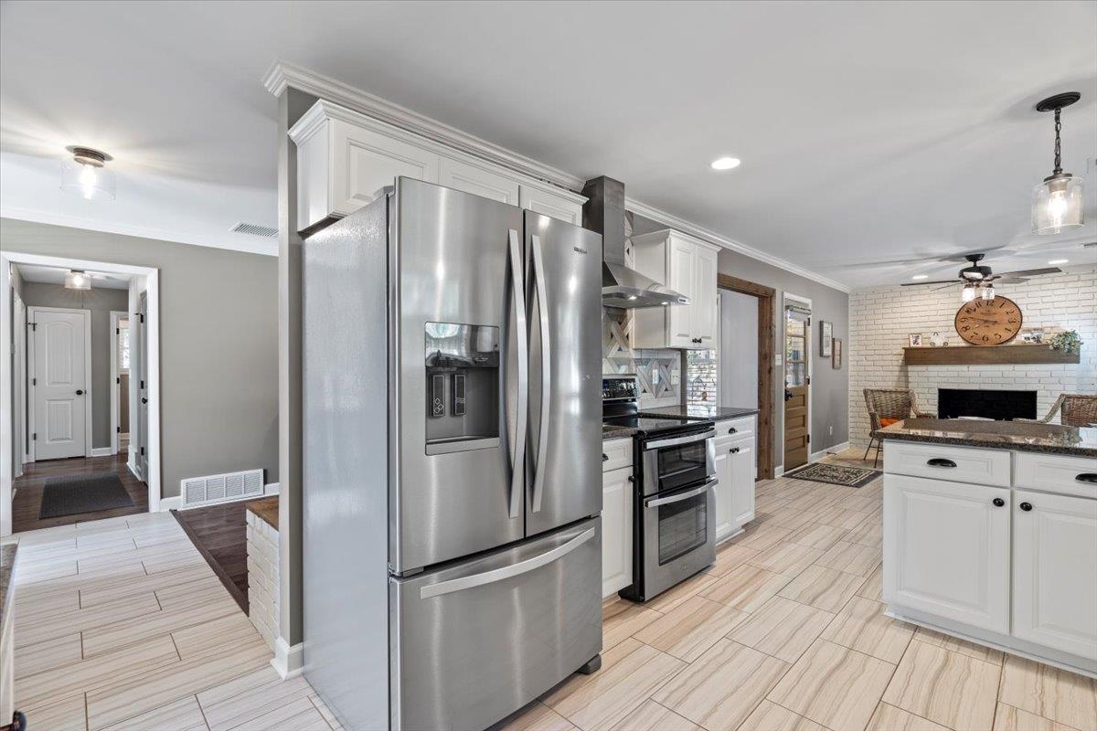 Kitchen with white cabinets, wall chimney exhaust hood, ceiling fan, appliances with stainless steel finishes, and brick wall