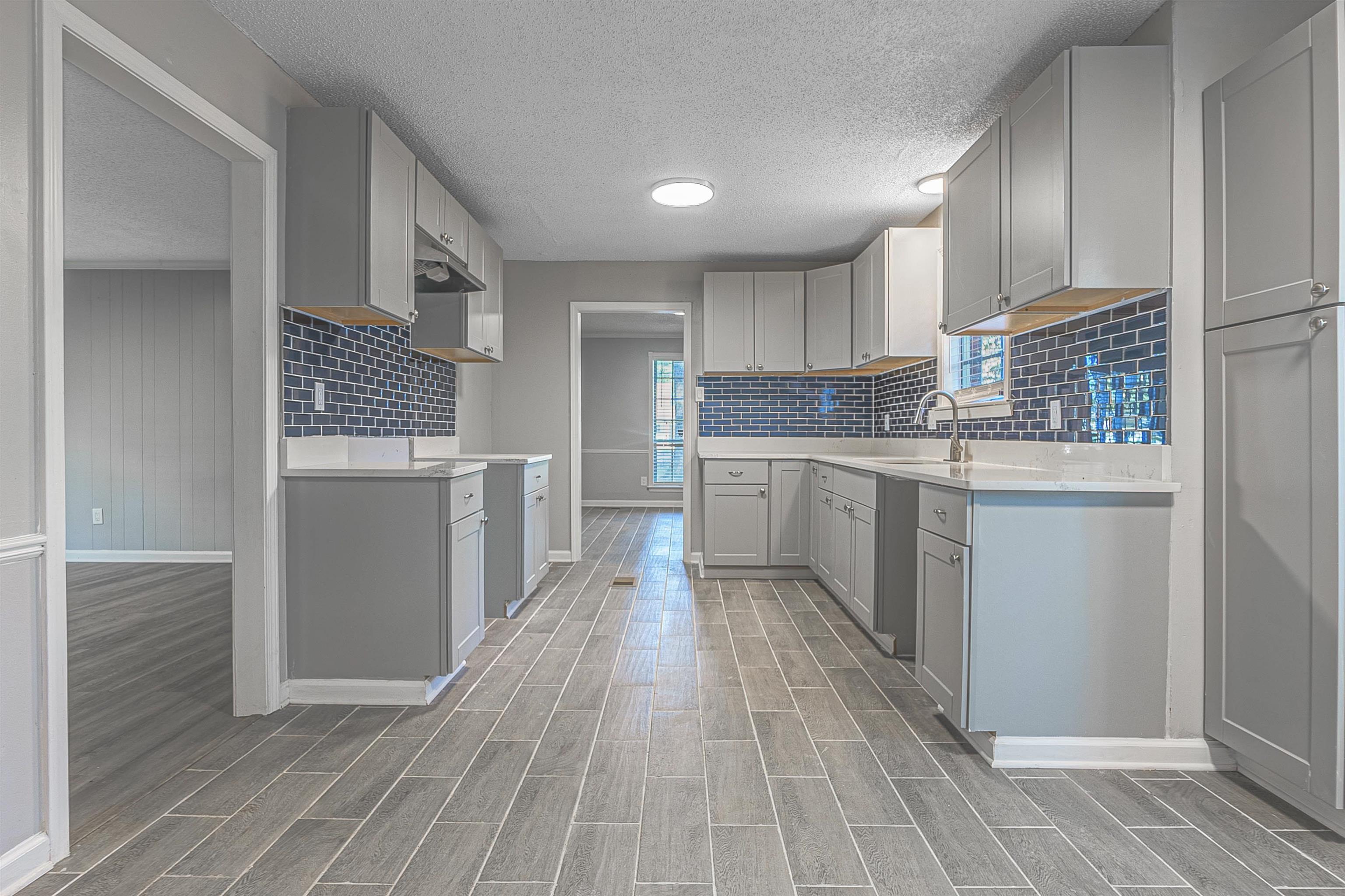 Kitchen featuring decorative backsplash, a textured ceiling, light wood-type flooring, and gray cabinets