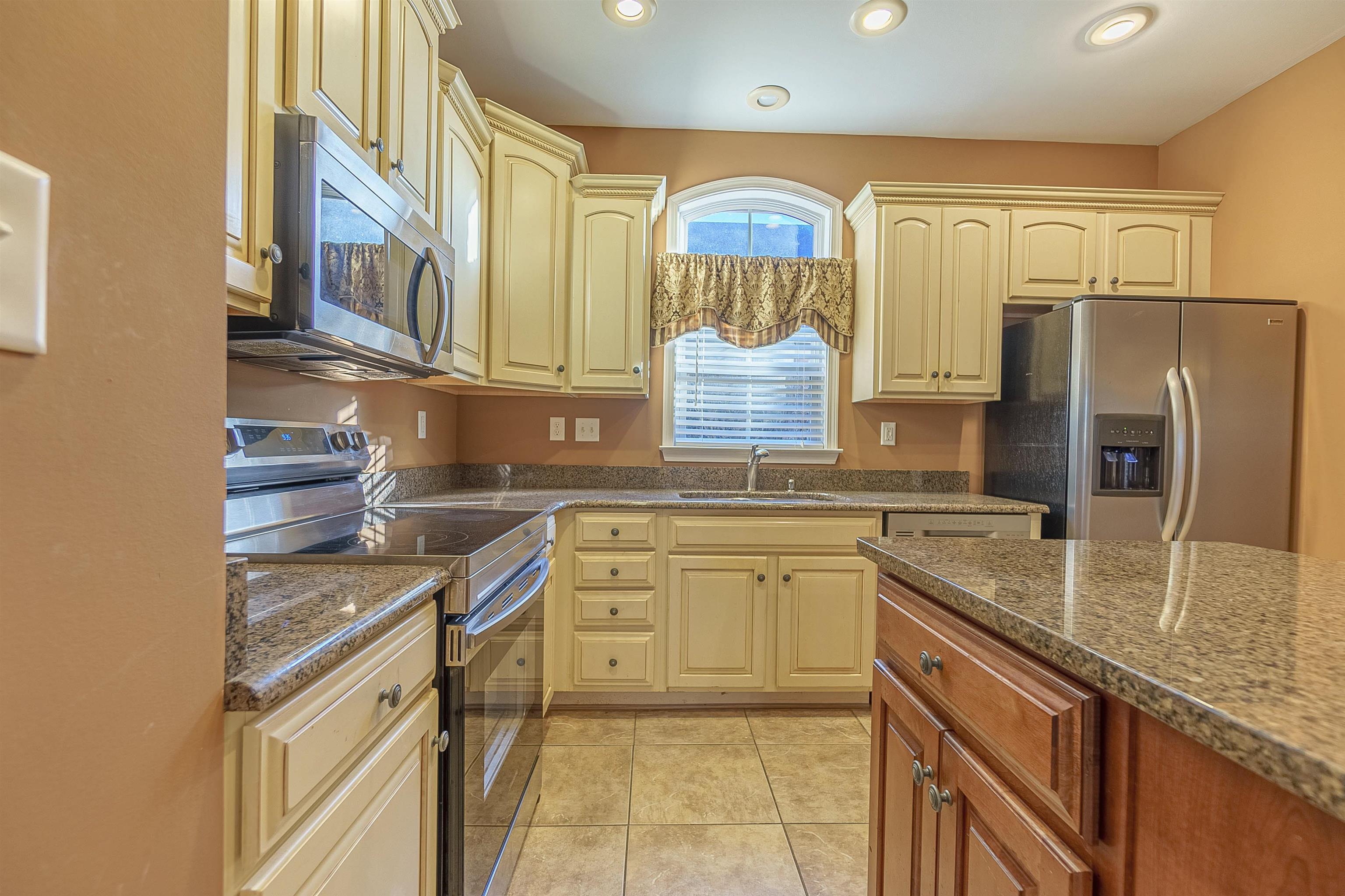 Kitchen with appliances with stainless steel finishes, light tile patterned floors, dark stone counters, and sink