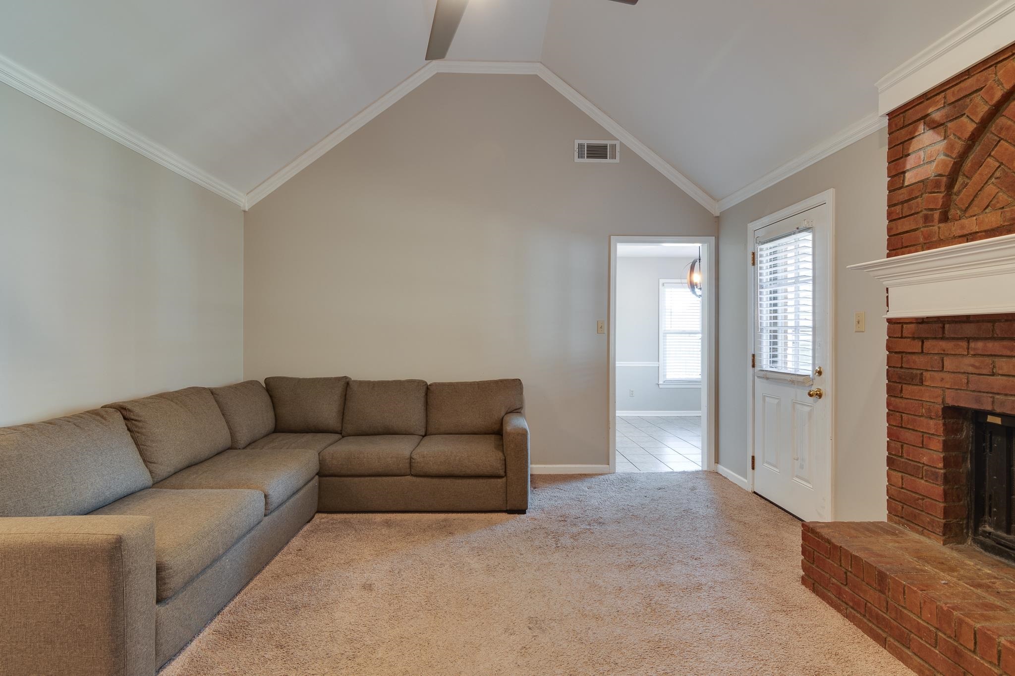 Carpeted living room with ornamental molding, a fireplace, and high vaulted ceiling