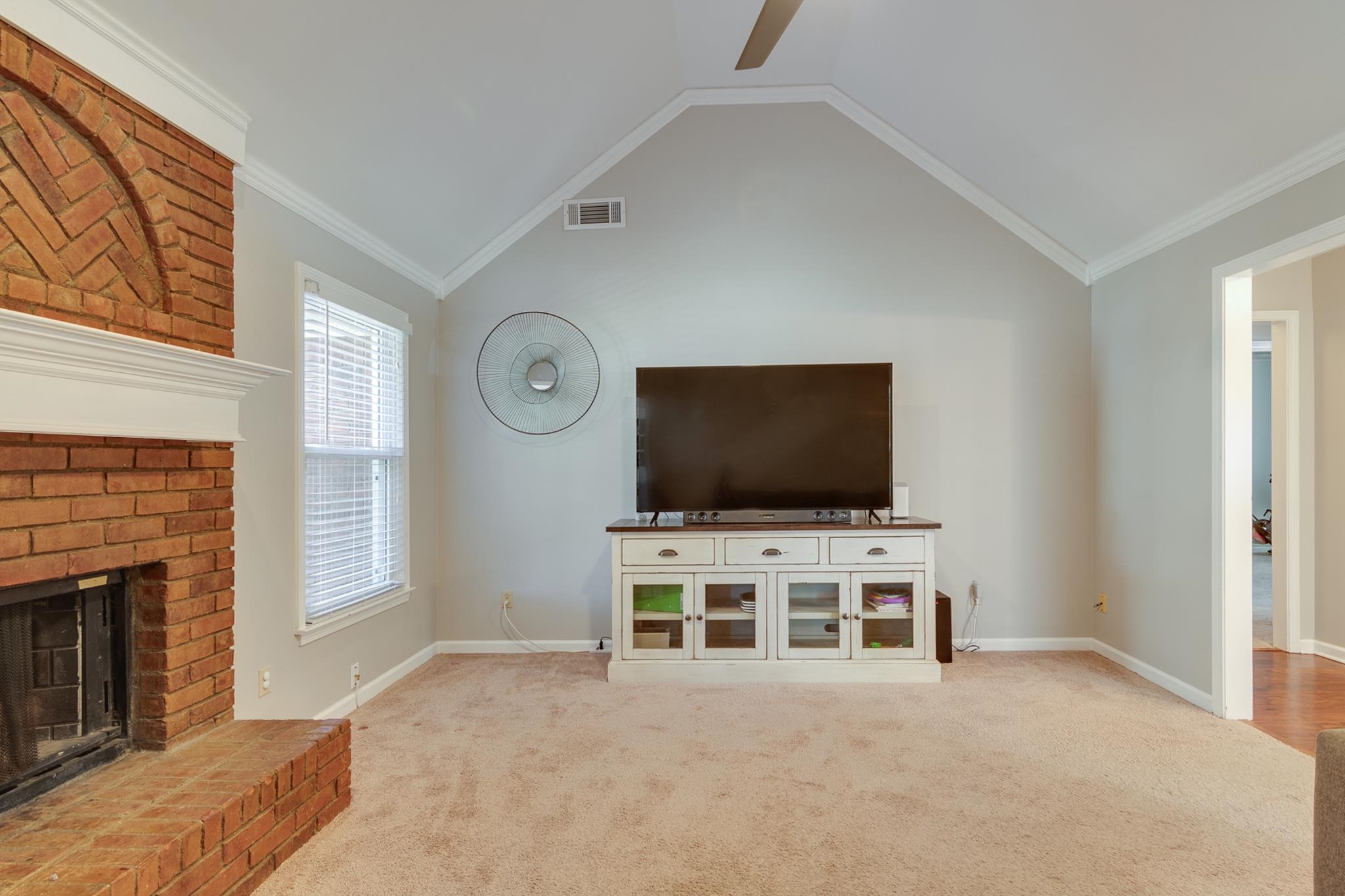 Unfurnished living room with light carpet, ornamental molding, ceiling fan, a fireplace, and lofted ceiling