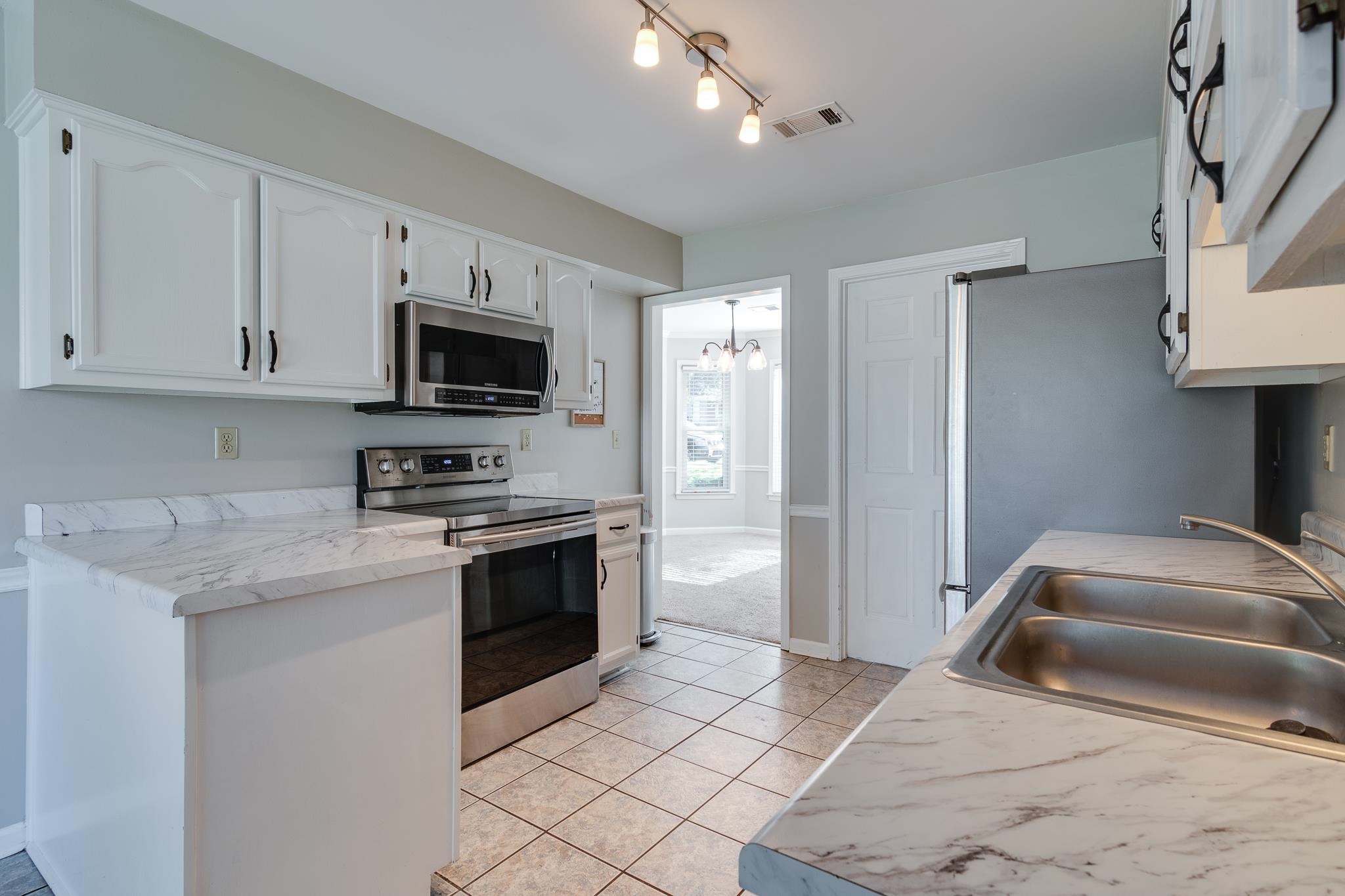 Kitchen featuring sink, light stone countertops, appliances with stainless steel finishes, light tile patterned flooring, and white cabinetry