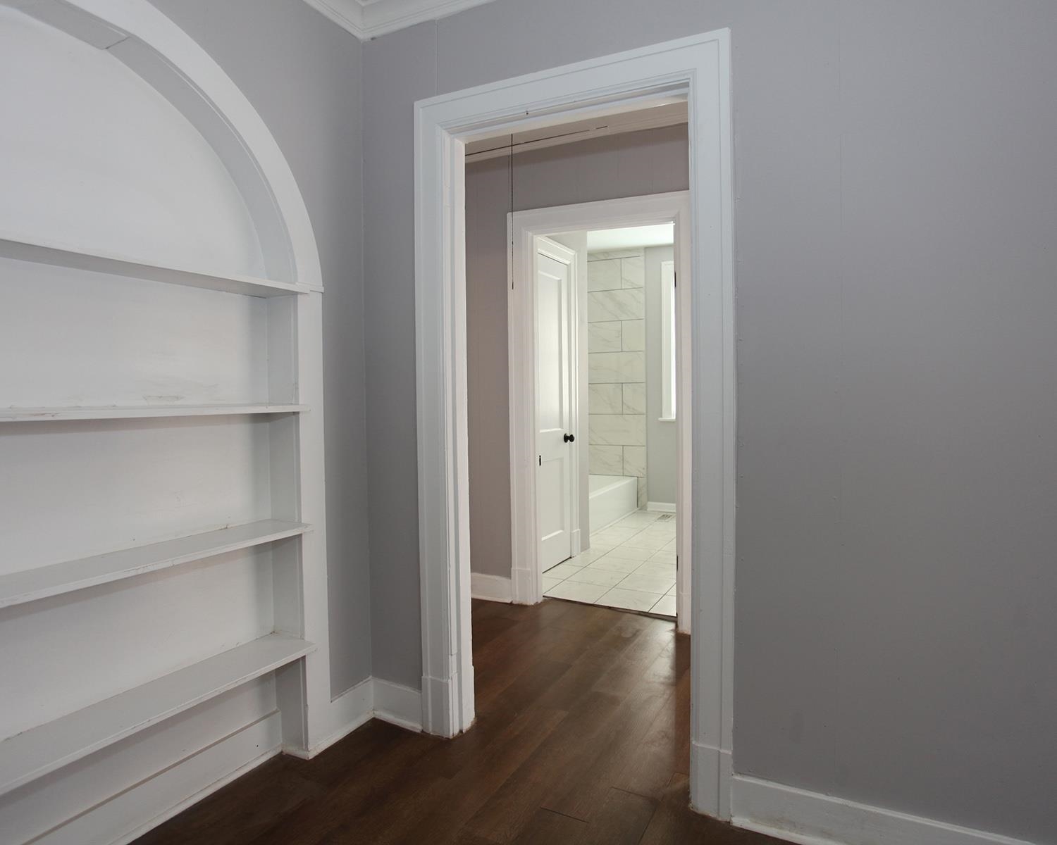 Corridor with built in shelves, dark hardwood / wood-style floors, and ornamental molding