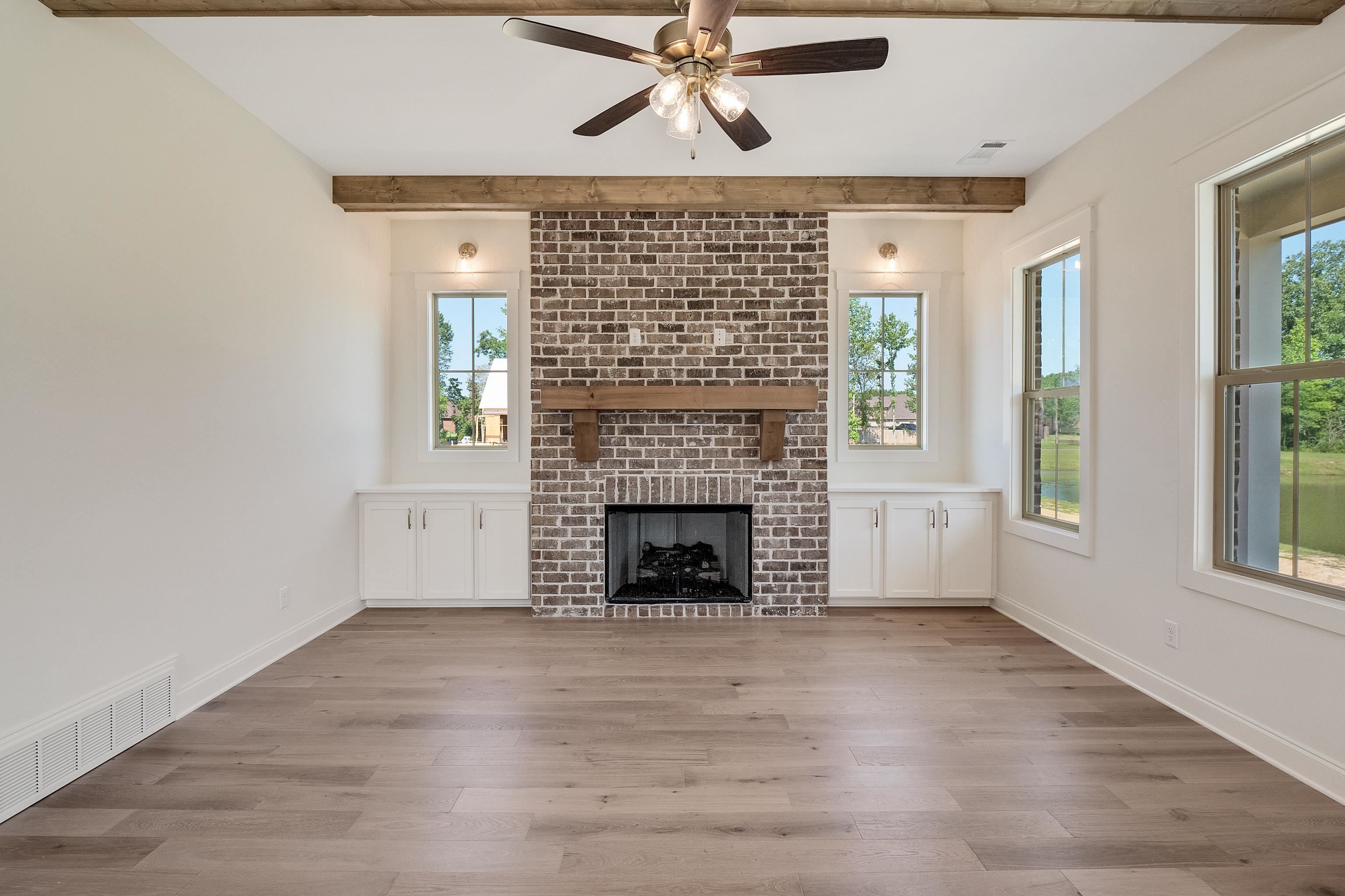 Unfurnished living room with beam ceiling, a brick fireplace, ceiling fan, and hardwood / wood-style flooring