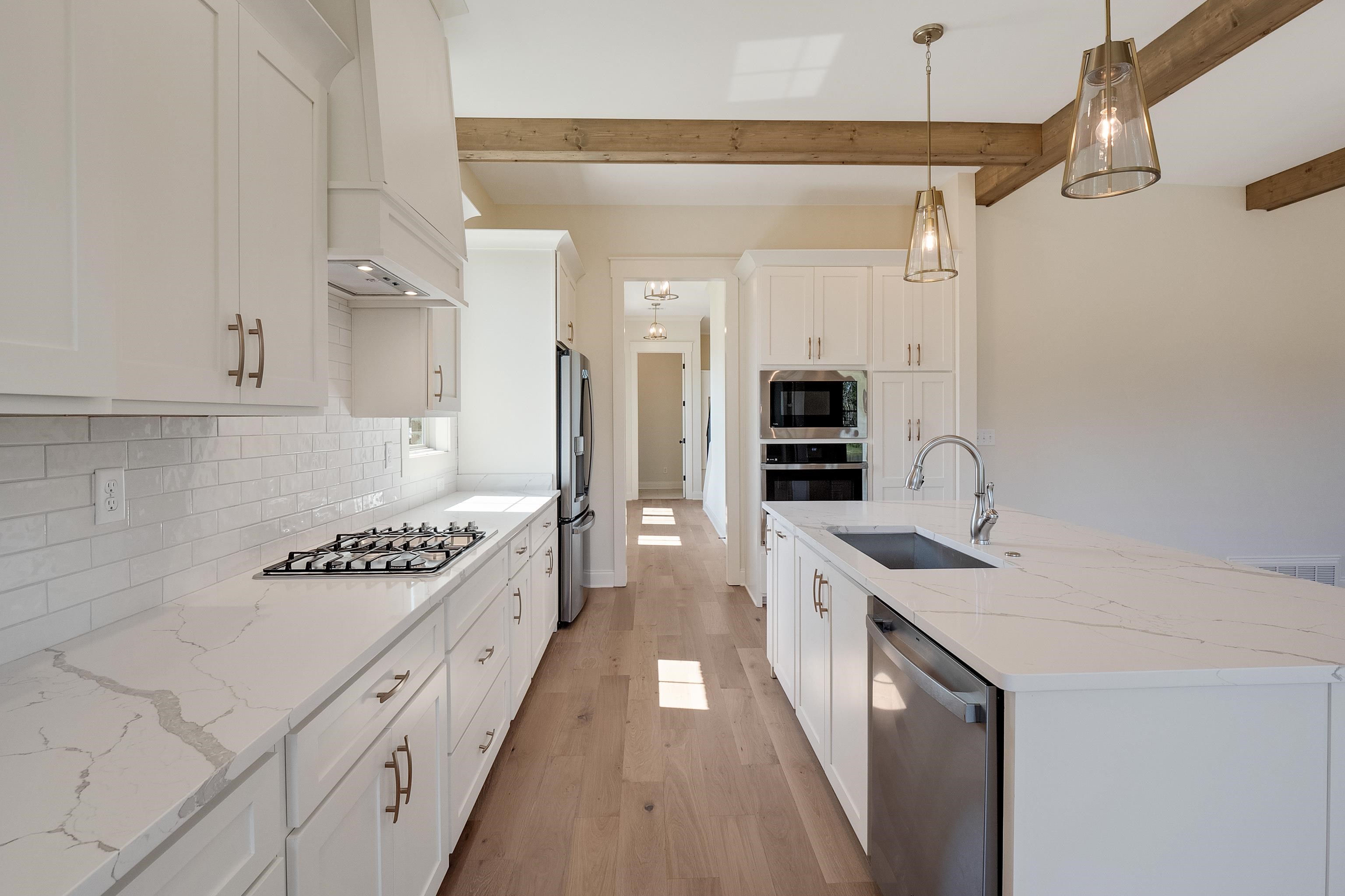 Kitchen with custom exhaust hood, stainless steel appliances, beam ceiling, decorative light fixtures, and white cabinetry