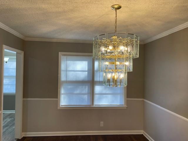 Unfurnished dining area featuring hardwood / wood-style flooring, a chandelier, a textured ceiling, and ornamental molding