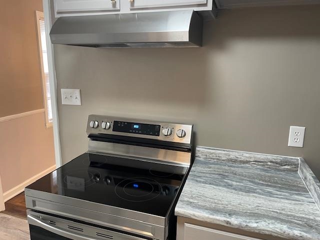 Kitchen featuring stainless steel range with electric stove top,Vinyl Plank waterproof floors, white cabinets, and Vent hood.