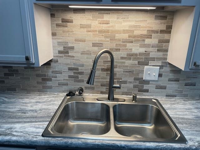 Interior details featuring decorative backsplash, blue cabinets, and sink