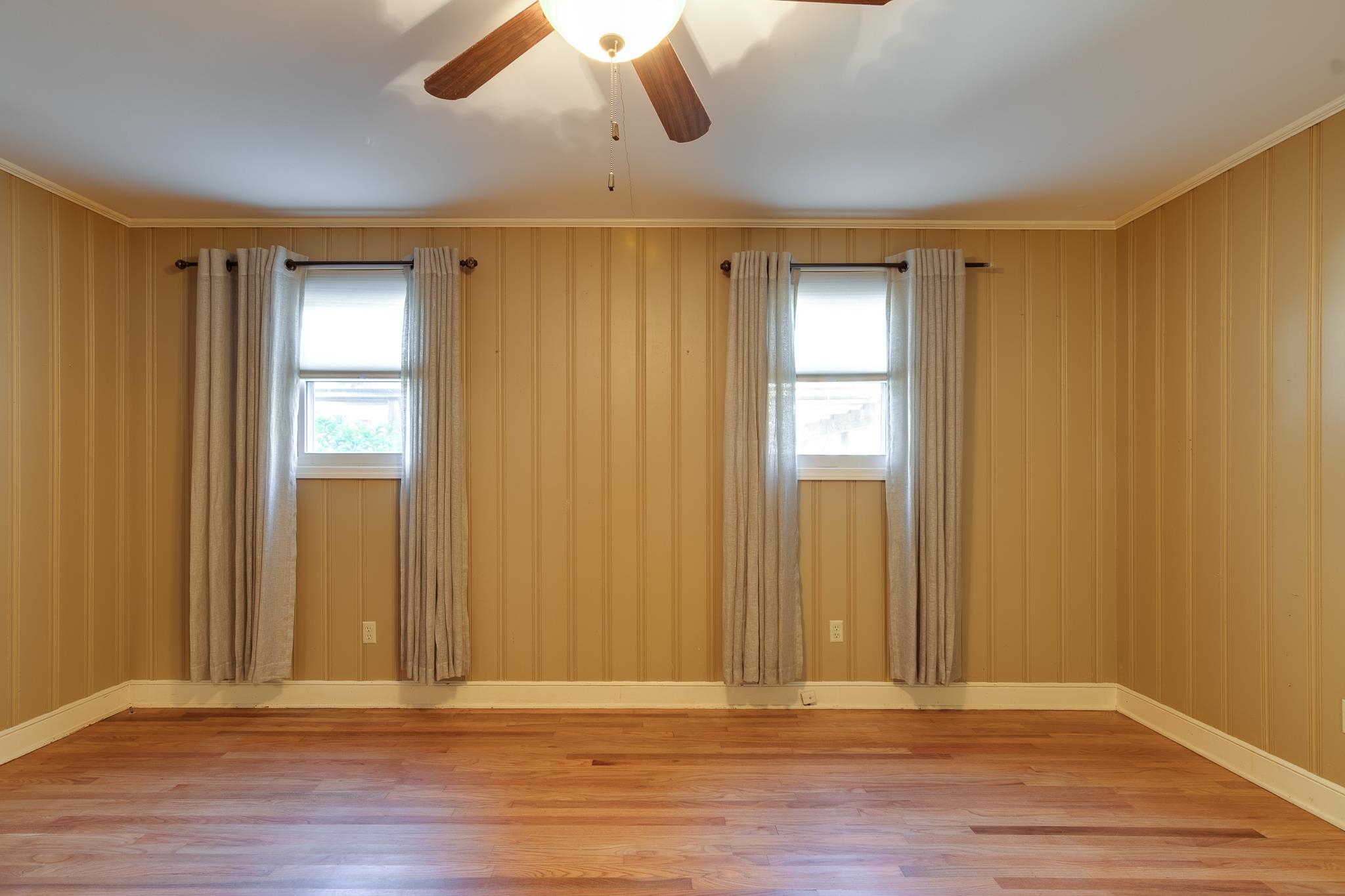 Empty room with ceiling fan, ornamental molding, wood walls, and hardwood / wood-style flooring