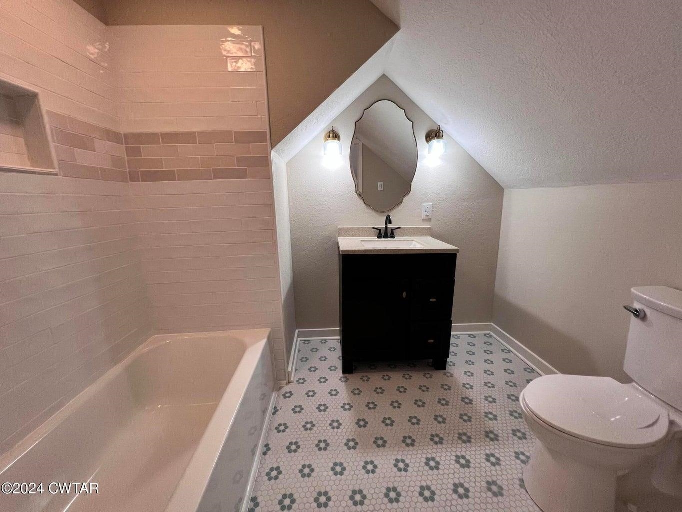 Full bathroom featuring tile patterned floors, a textured ceiling, vanity, vaulted ceiling, and toilet