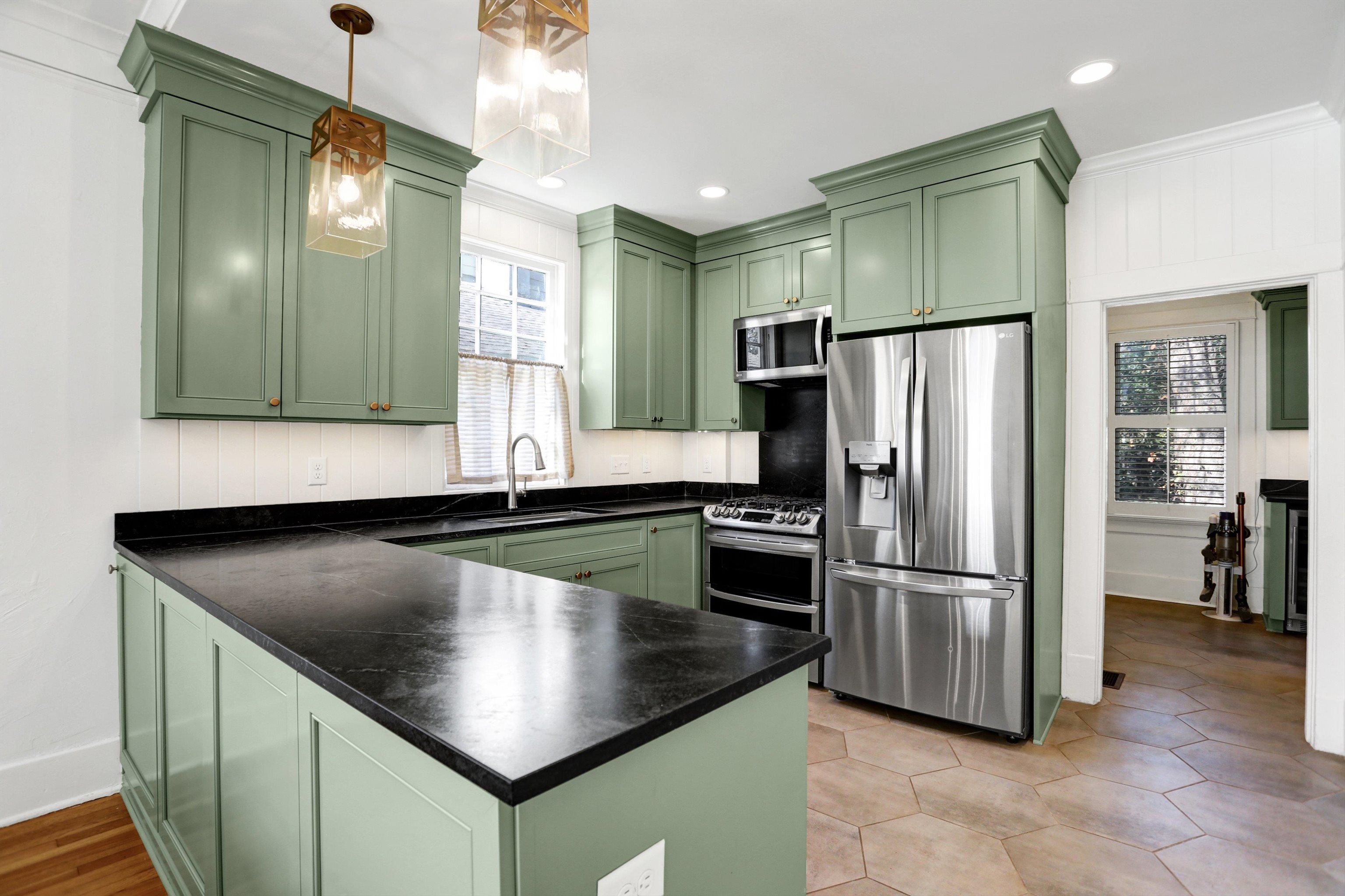 Kitchen with green cabinets, sink, decorative light fixtures, kitchen peninsula, and stainless steel appliances