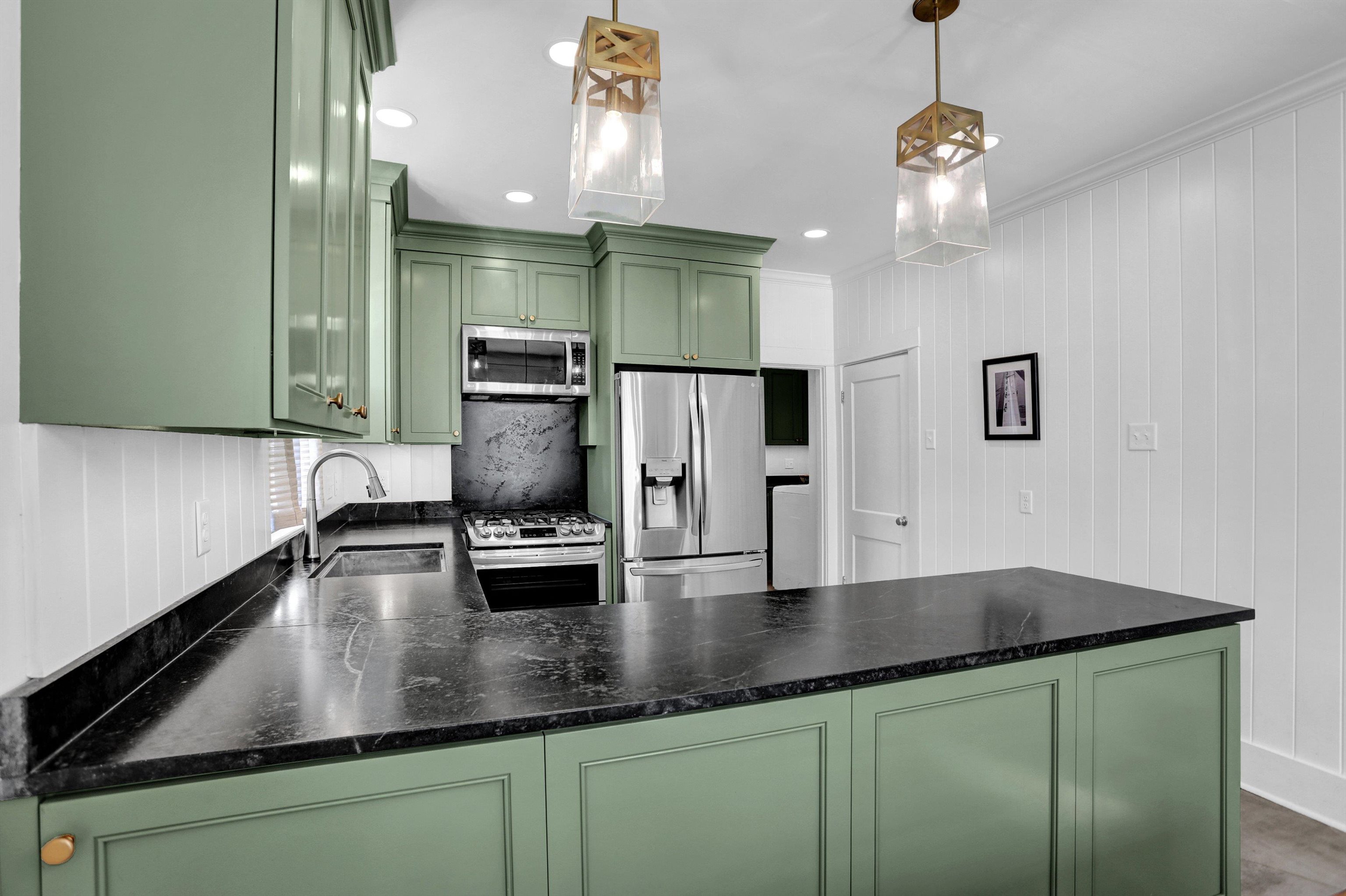 Kitchen featuring green cabinets, sink, hanging light fixtures, and appliances with stainless steel finishes