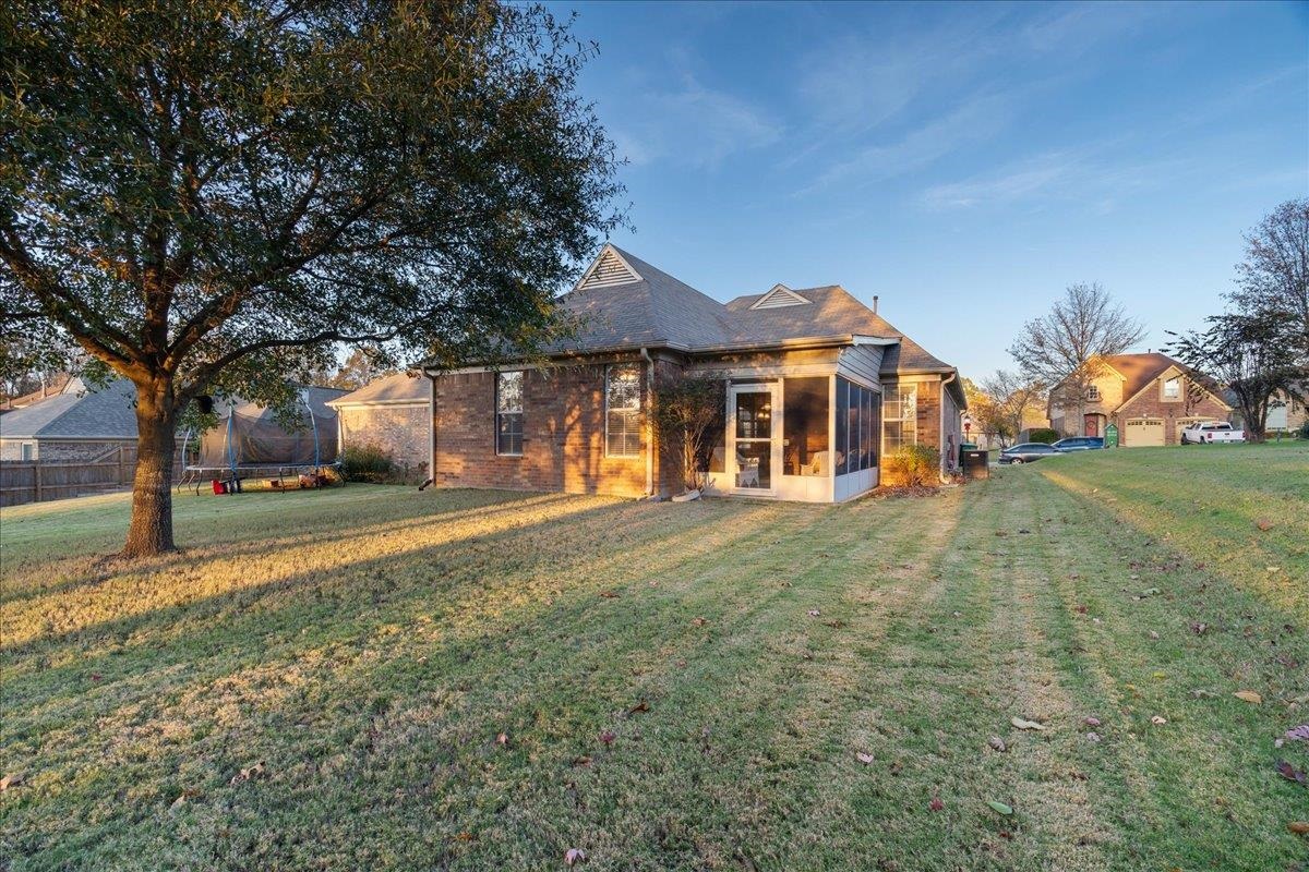 Rear view of house featuring a yard, a trampoline, and a sunroom