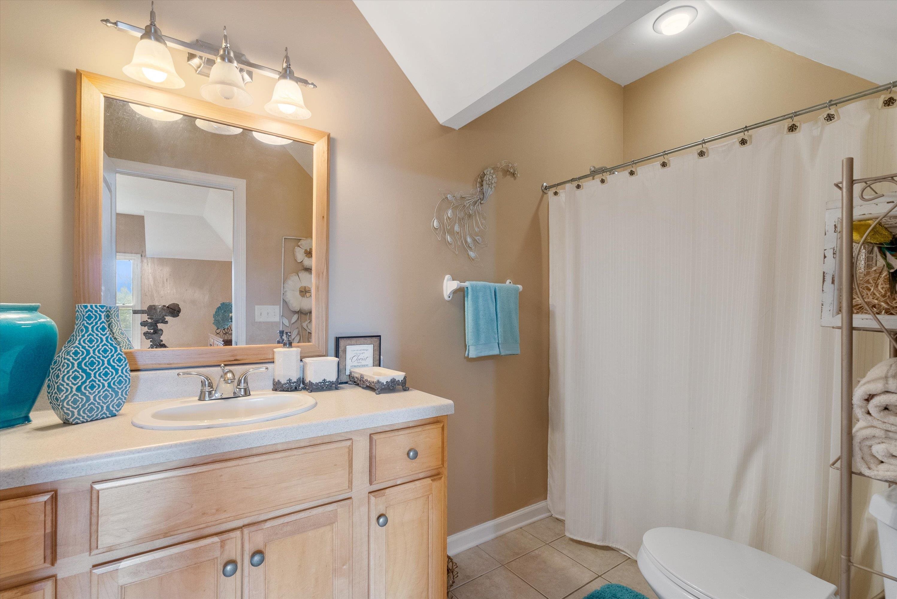 Bathroom featuring tile patterned flooring, vanity, toilet, and vaulted ceiling