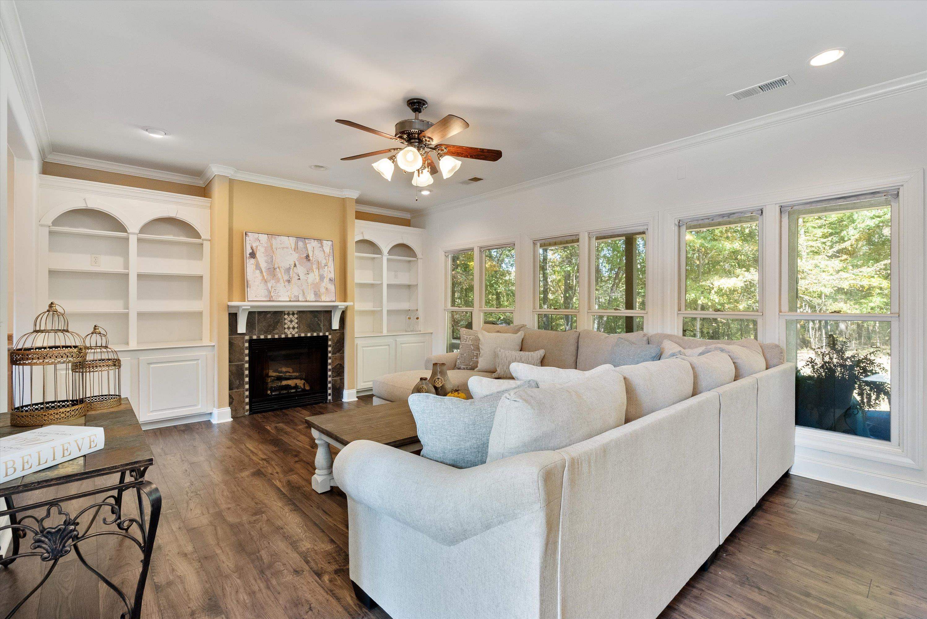 Living room with dark hardwood / wood-style floors, ceiling fan, ornamental molding, and a fireplace