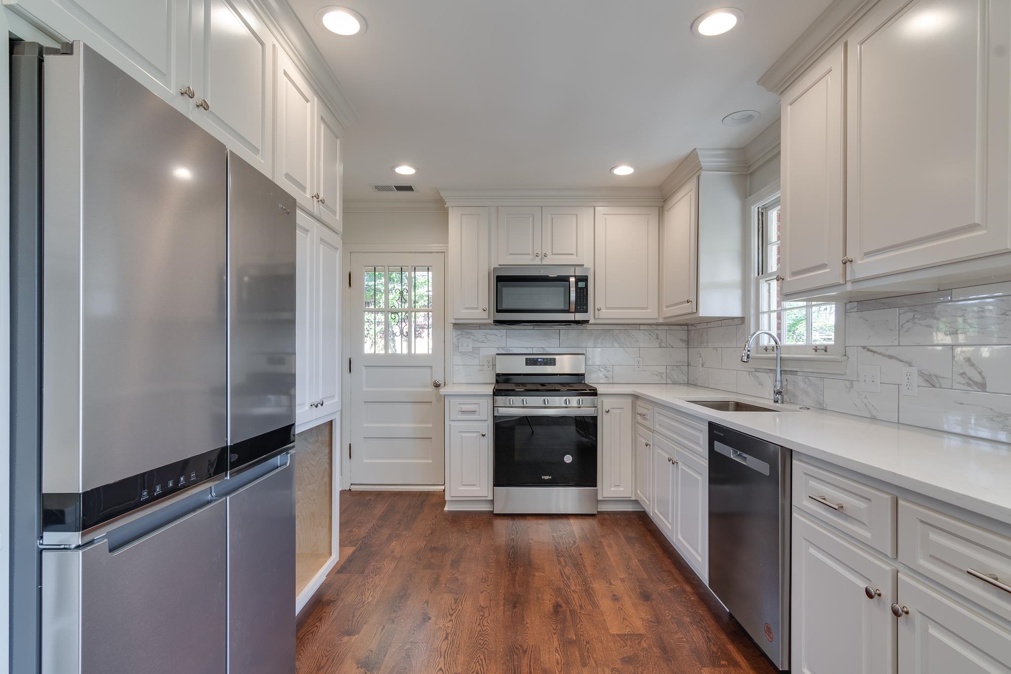 Kitchen with white cabinets, ornamental molding, stainless steel appliances, and a healthy amount of sunlight