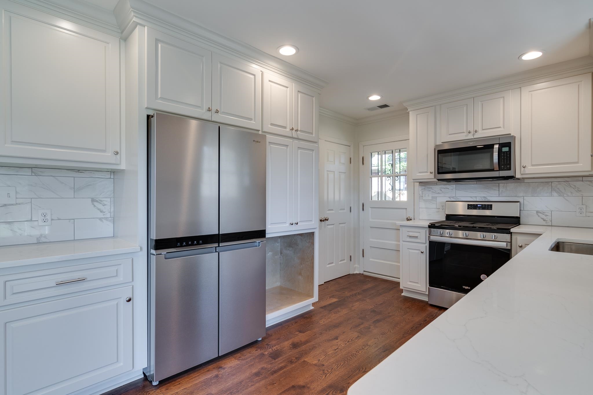 Kitchen with white cabinetry, crown molding, dark wood-type flooring, and appliances with stainless steel finishes