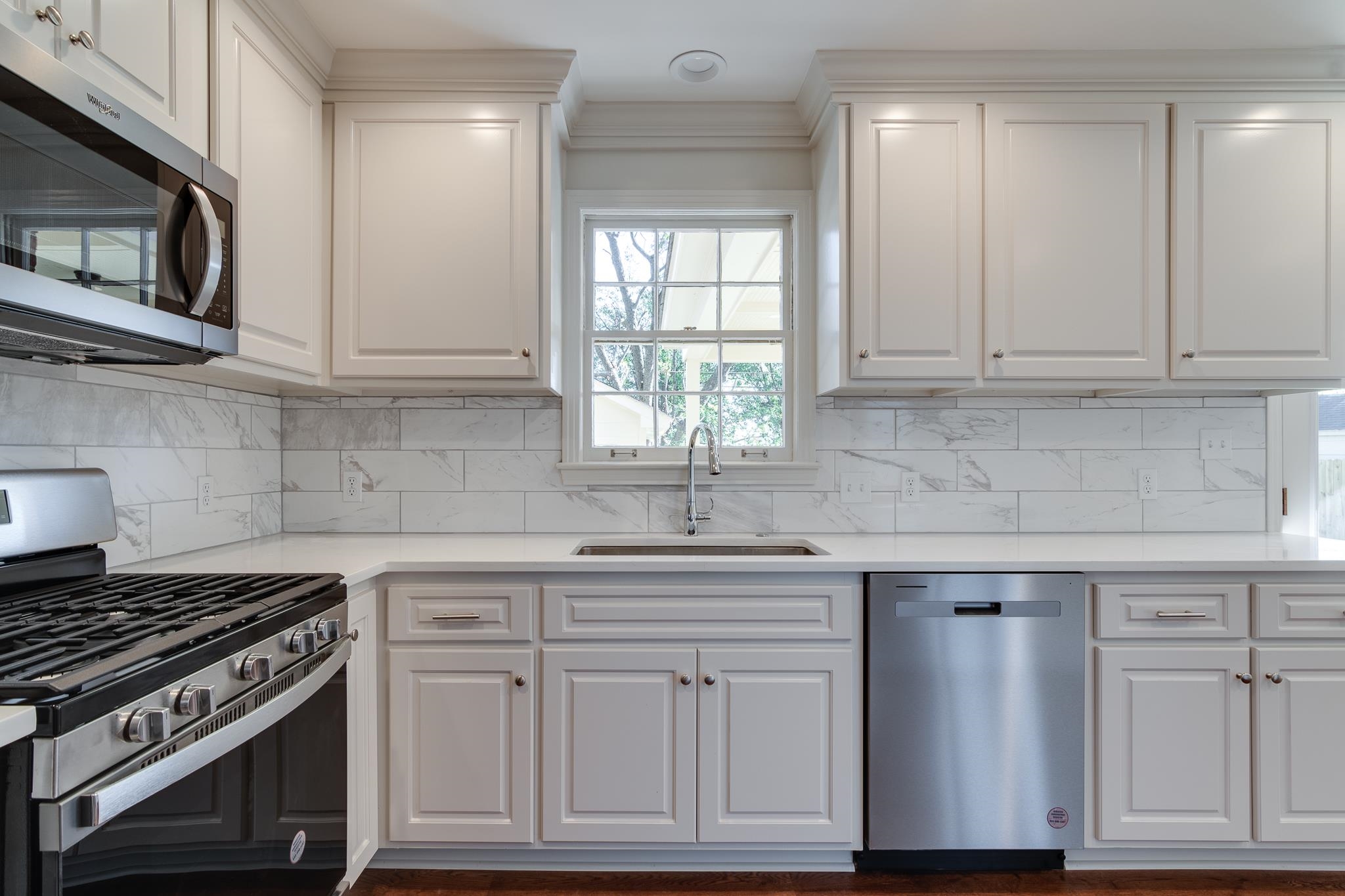 Kitchen with decorative backsplash, white cabinetry, sink, and appliances with stainless steel finishes