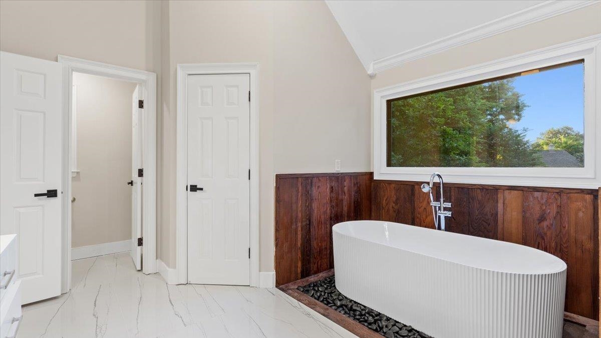 Bathroom featuring wood walls, a bath, and vaulted ceiling