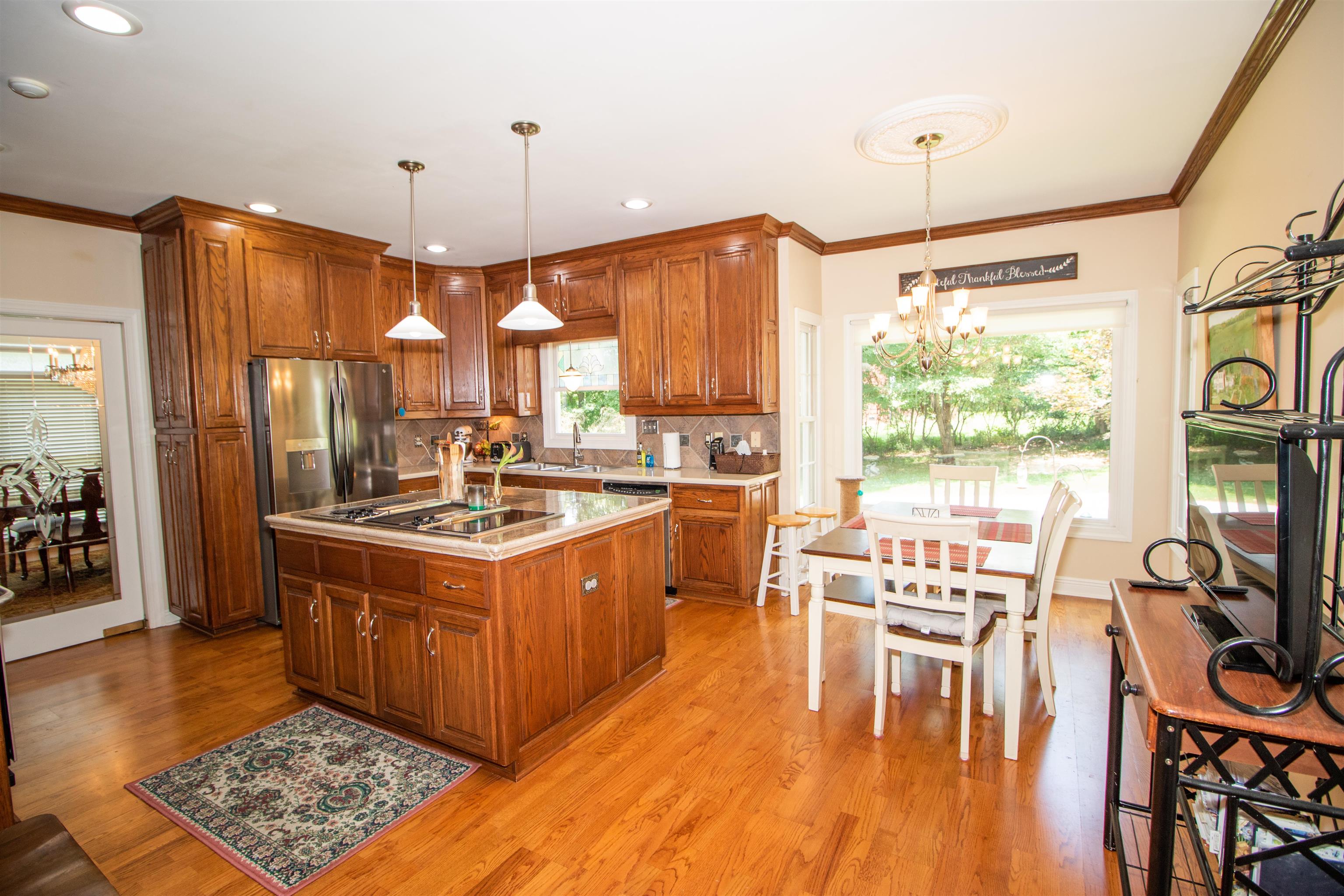 Kitchen featuring backsplash, an inviting chandelier, light wood-type flooring, an island with sink, and decorative light fixtures