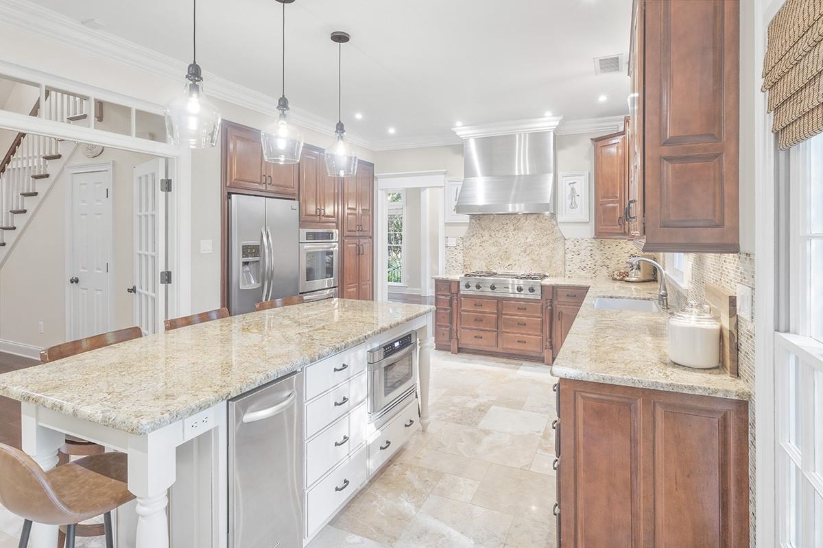 Kitchen featuring light stone countertops, sink, wall chimney range hood, a kitchen island, and appliances with stainless steel finishes