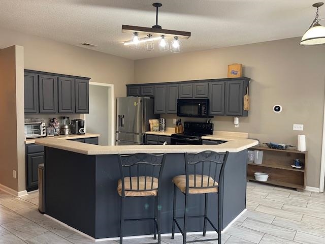 Kitchen featuring kitchen peninsula, a kitchen breakfast bar, gray cabinetry, black appliances, and decorative light fixtures