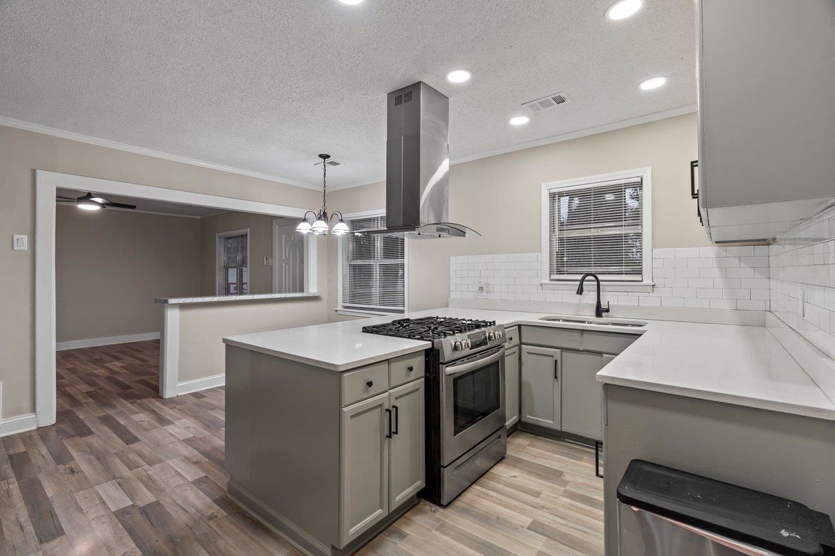 Kitchen with sink, high end stainless steel range, decorative light fixtures, kitchen peninsula, and island exhaust hood