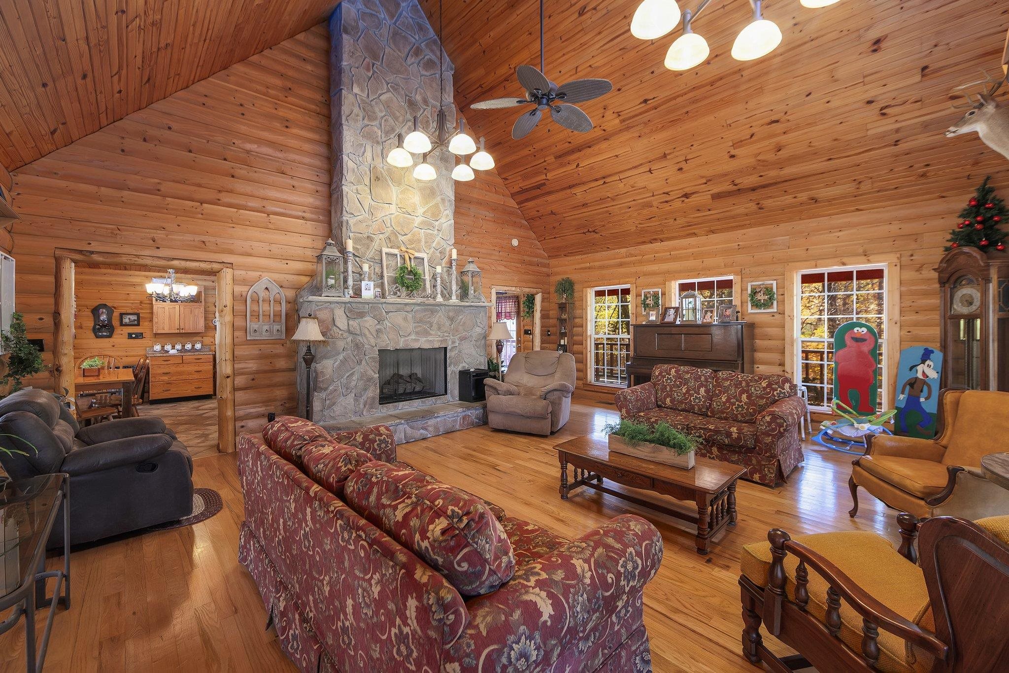 Living room with ceiling fan, a stone fireplace, light hardwood / wood-style flooring, high vaulted ceiling, and wood walls