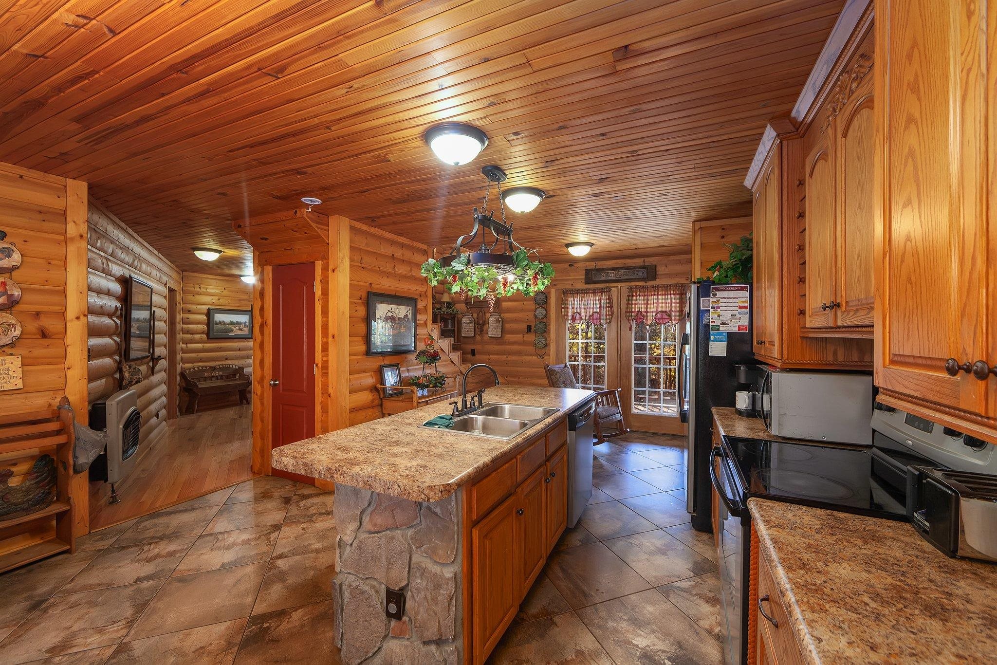 Kitchen featuring sink, log walls, pendant lighting, a kitchen island with sink, and appliances with stainless steel finishes
