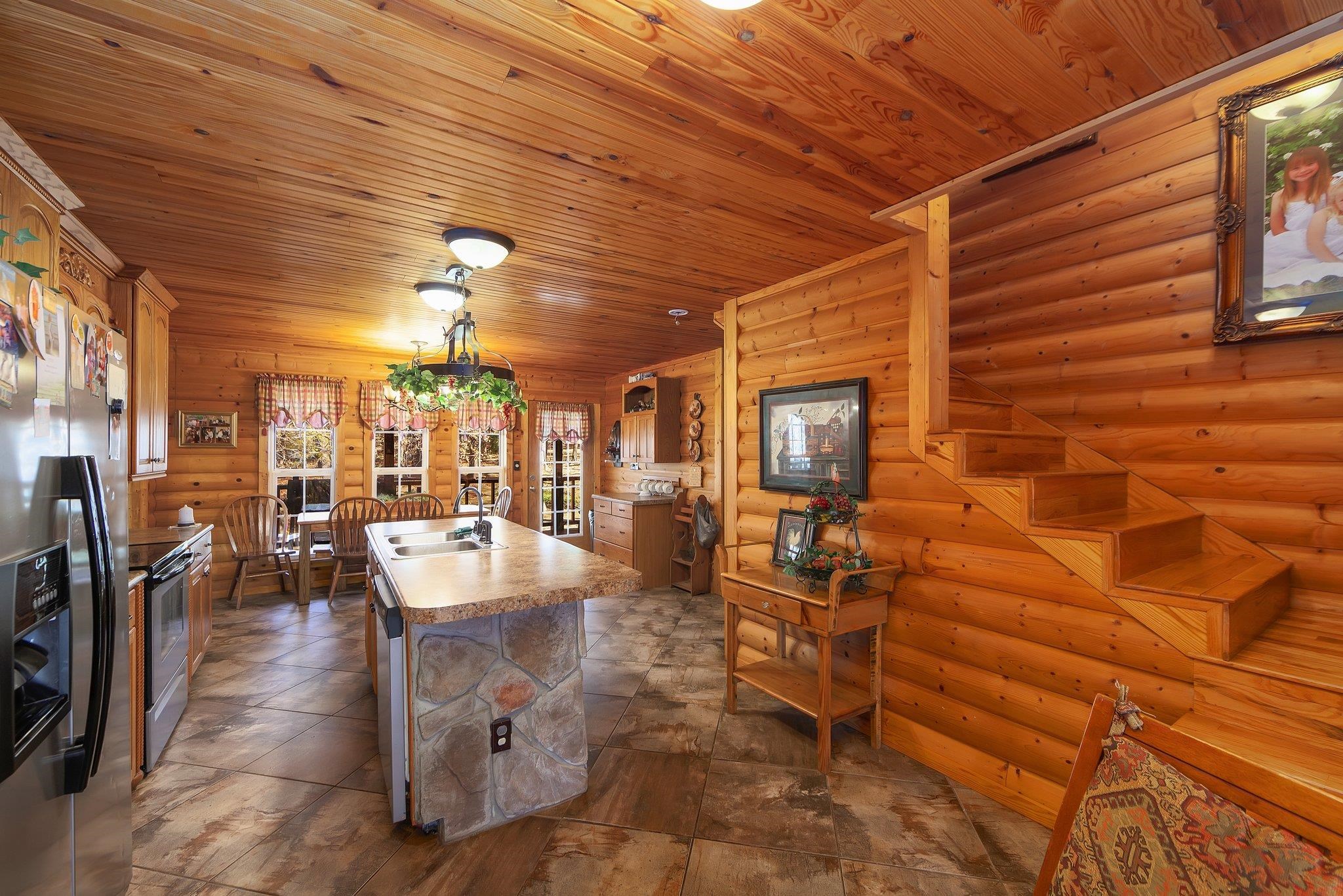 Kitchen with rustic walls, pendant lighting, a kitchen island with sink, wood ceiling, and appliances with stainless steel finishes