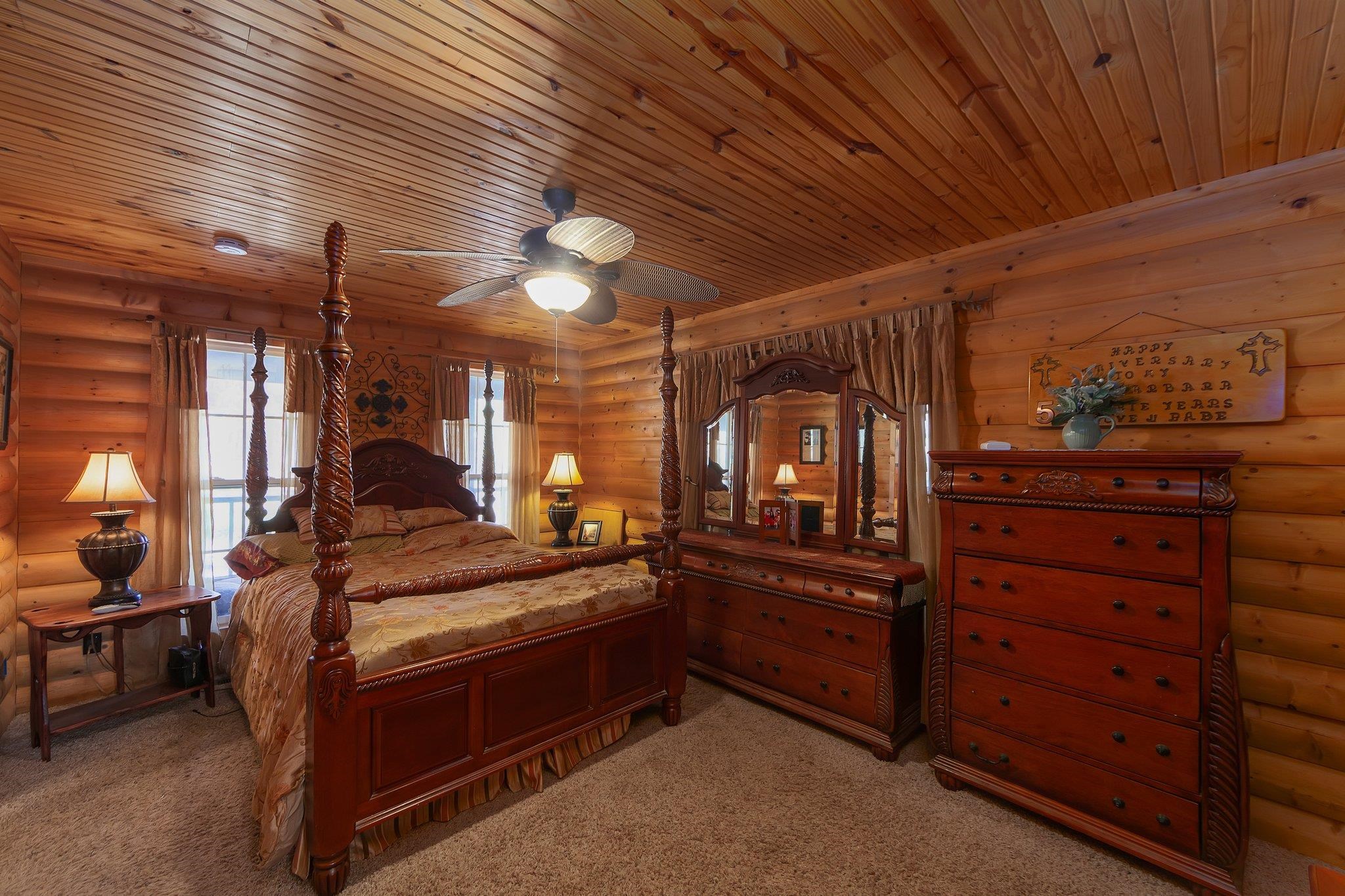 Carpeted bedroom featuring rustic walls, ceiling fan, and wood ceiling